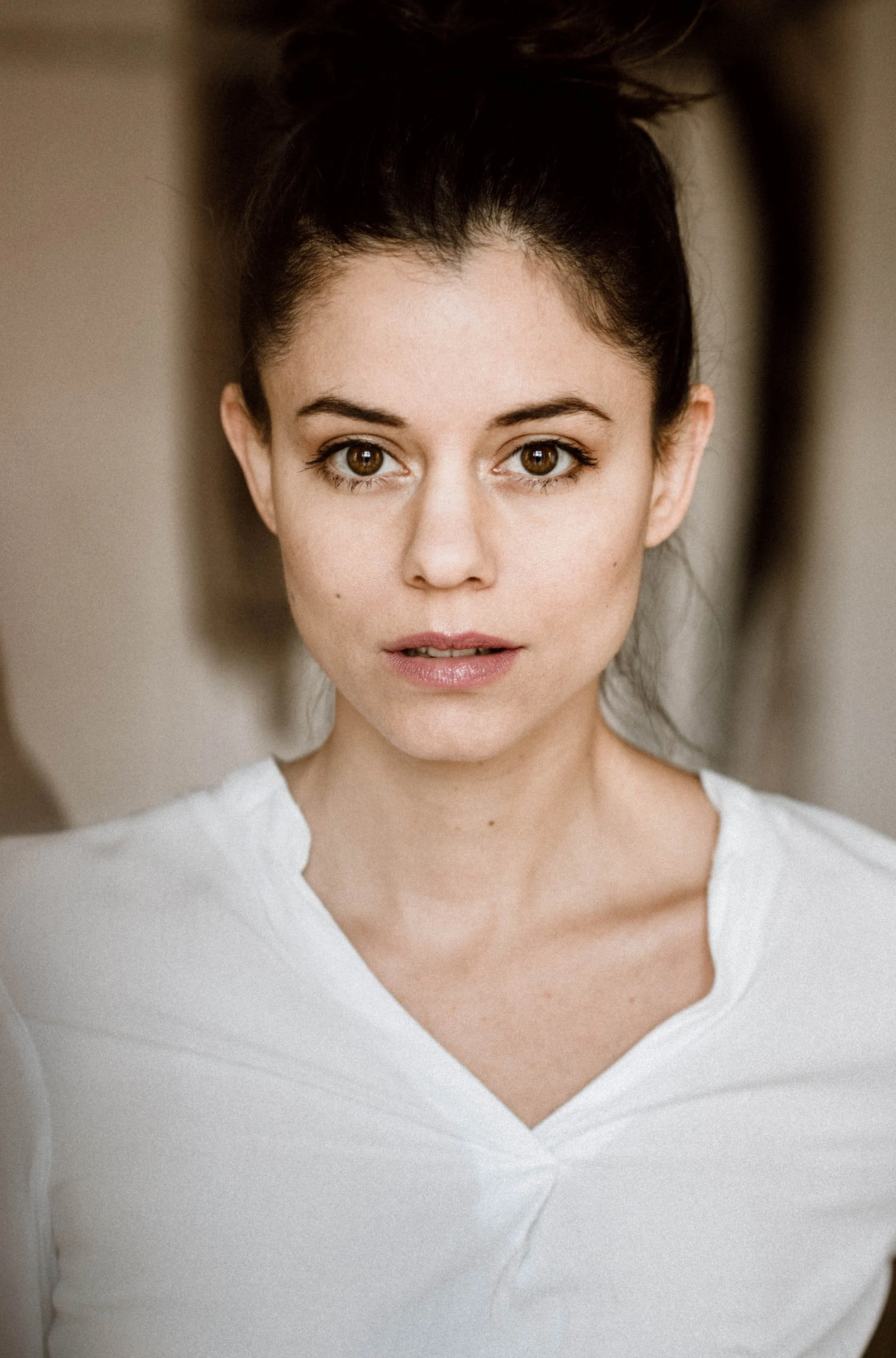 Nahaufnahme eines jungen Frau mit braunen Augen, dunklen Haaren, die zu einem hohen Pferdeschwanz gebunden sind, trägt ein weißes Shirt und schaut direkt in die Kamera.