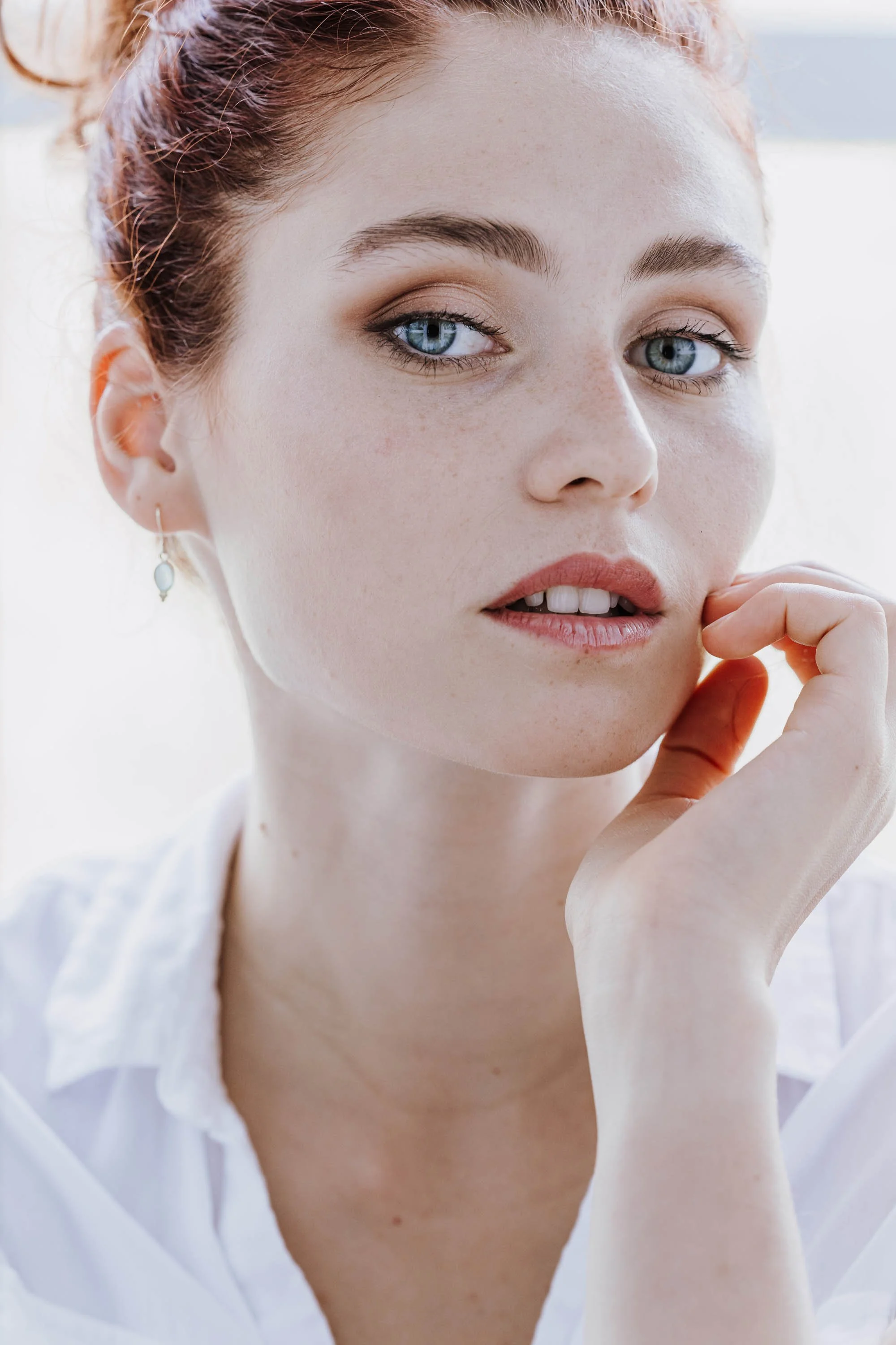 Nahaufnahme eines jungen Mädchens mit rotem Haar, blauen Augen und Freckles, das leicht die Lippe berührt.