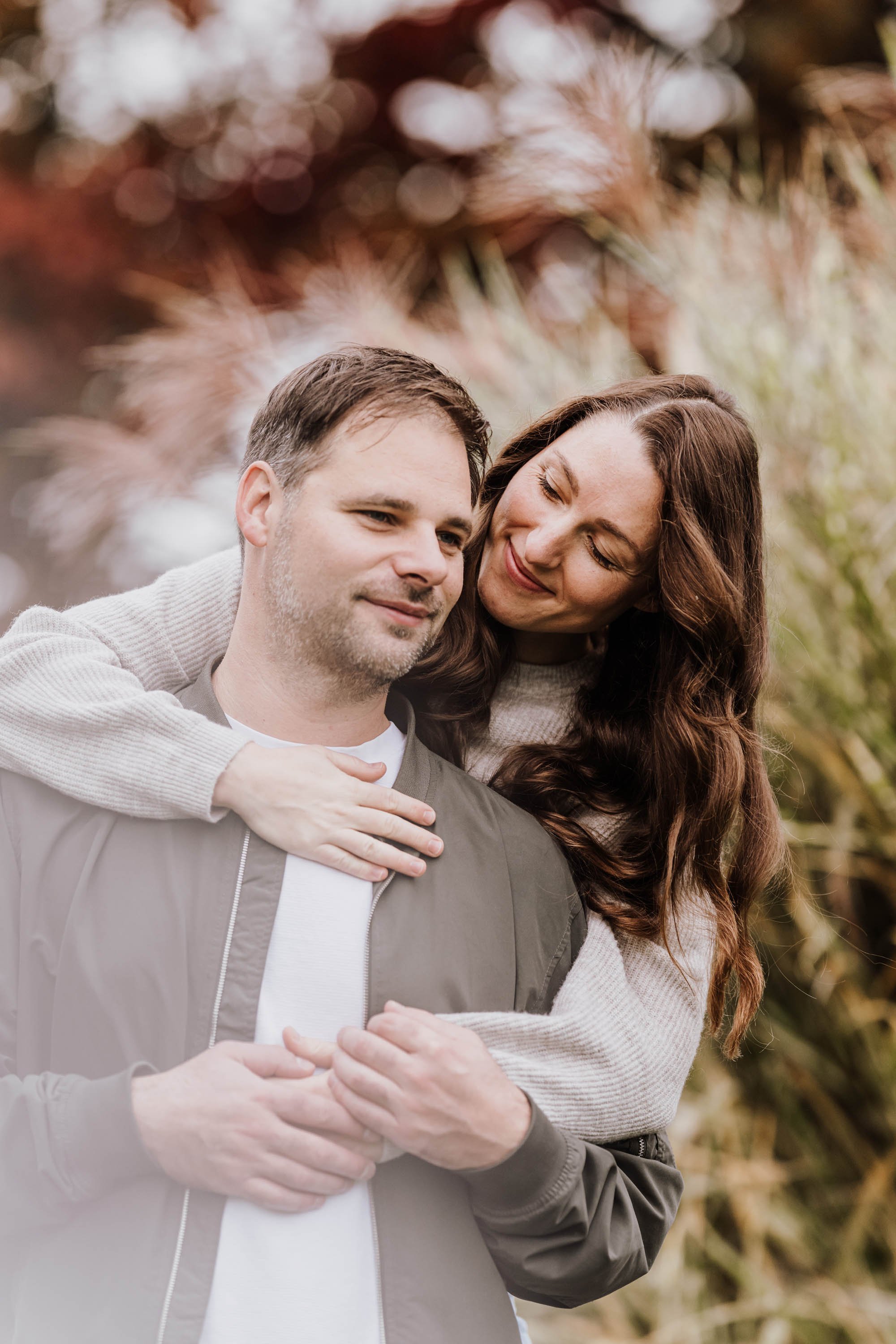 Ein glückliches Paar, das im Freien umarmt und lächelt, mit herbstlichen Bäumen im Hintergrund.