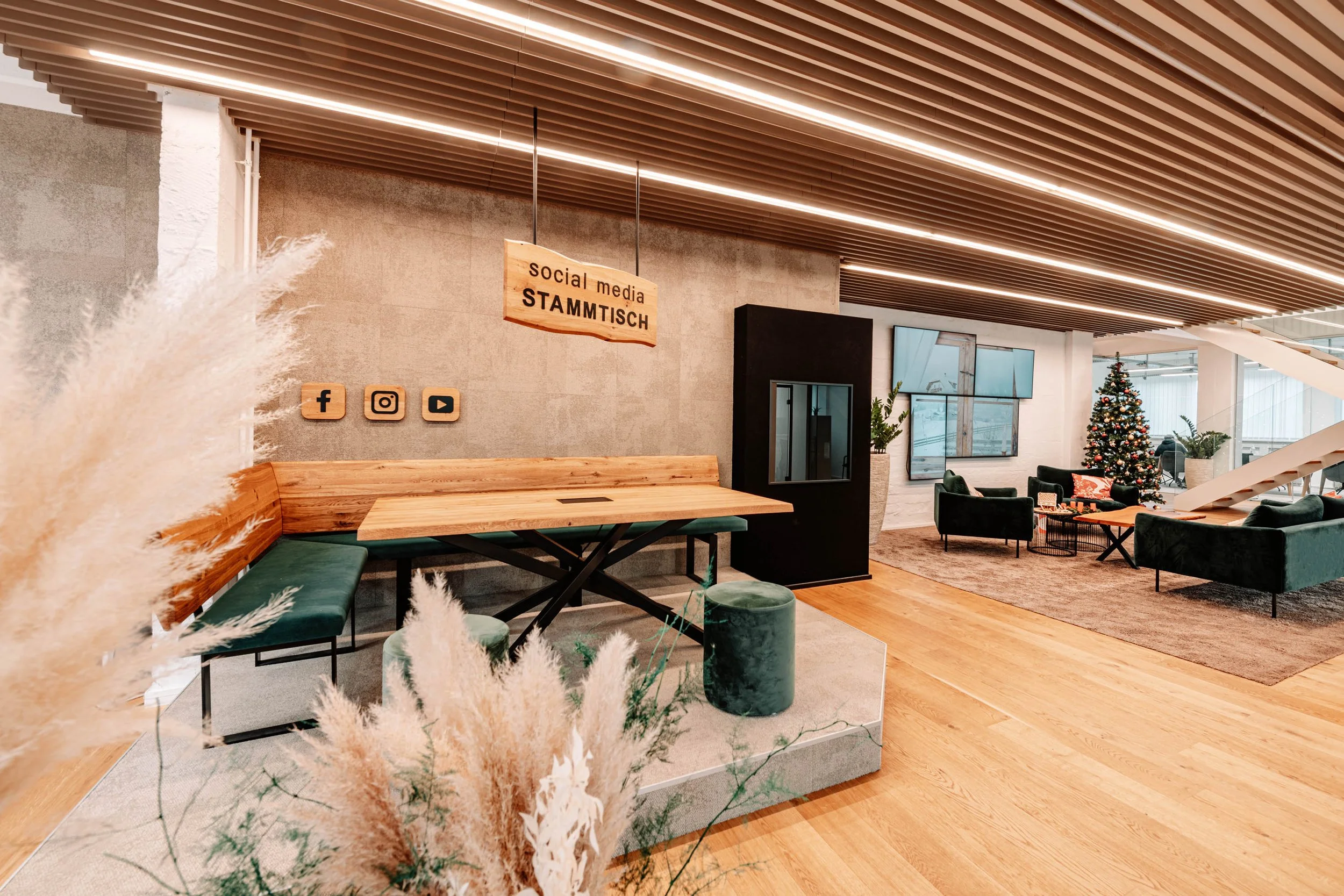 Moderner, gemütlicher Indoor-Treffpunkt mit Weihnachtsbaum, Sofas, Fernsehern und sozialen Medien Icons an der Wand, Holzdecke und Holzboden.