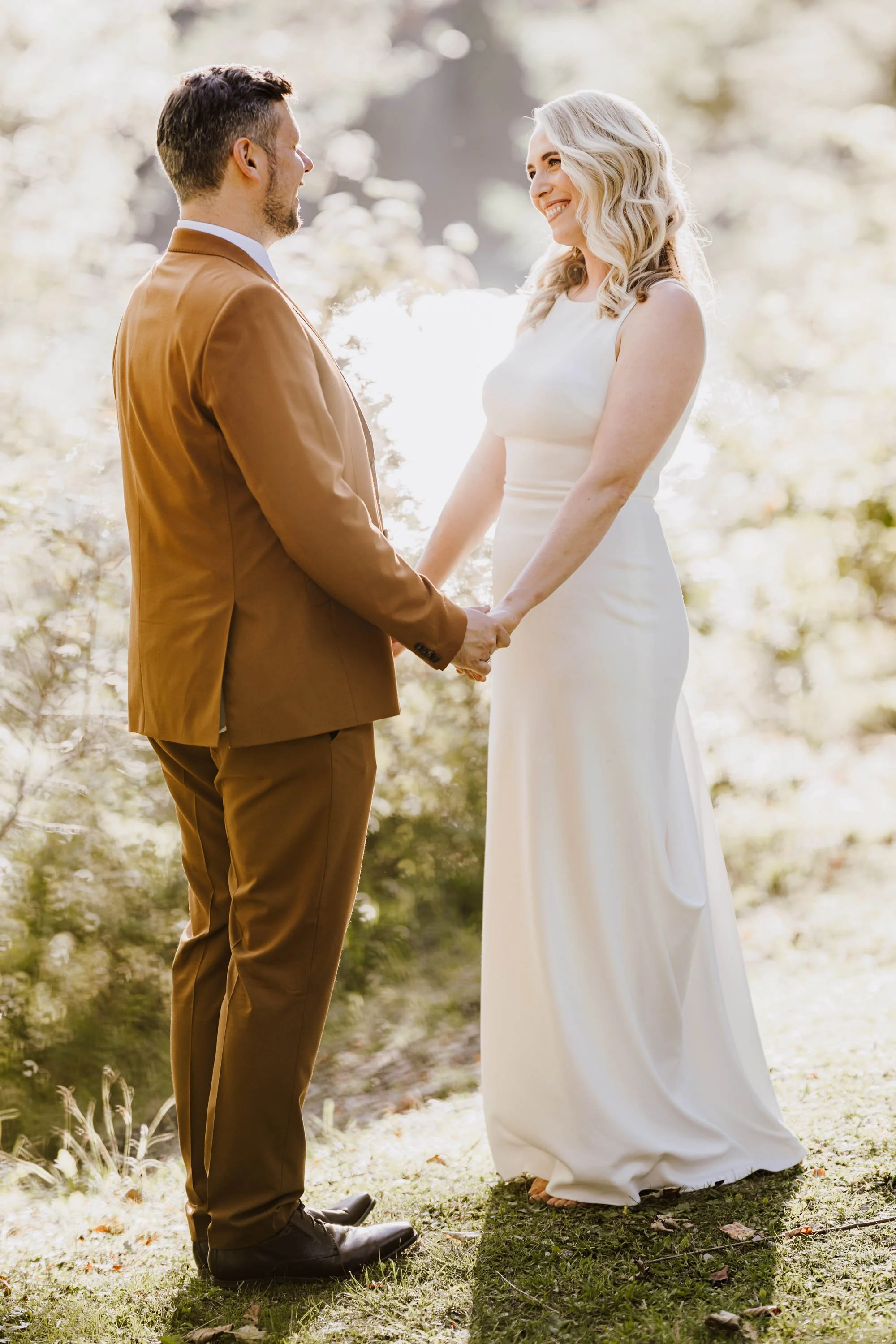 Ein Paar bei einer Hochzeitszeremonie im Freien, das sich an den Händen hält und sich liebevoll ansieht, mit natürlichem Licht im Hintergrund.