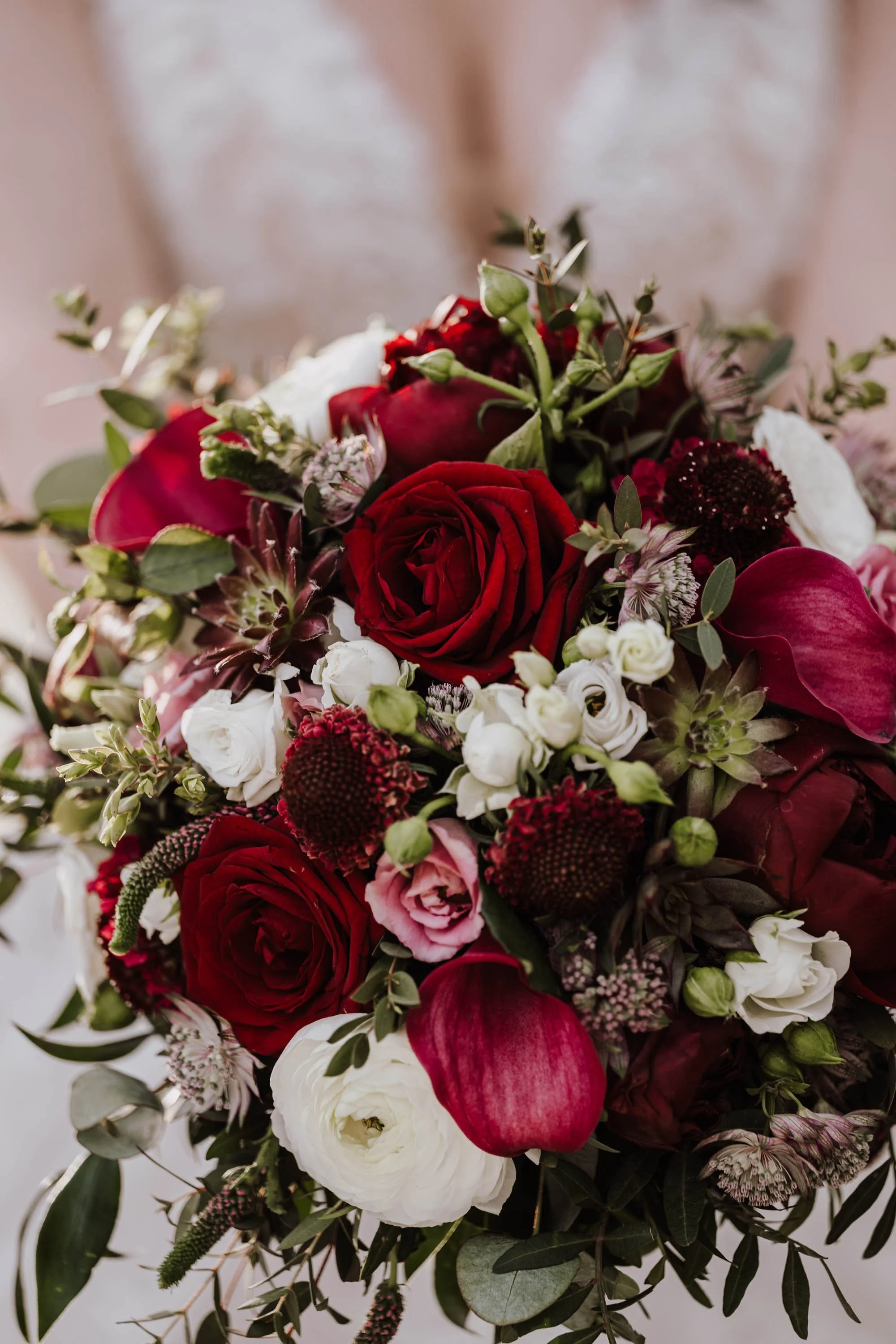 Ein Blumenstrauß mit roten, weißen und pinken Blumen, darunter Rosen und Calla-Lilien, sowie grünem Blätterwerk.