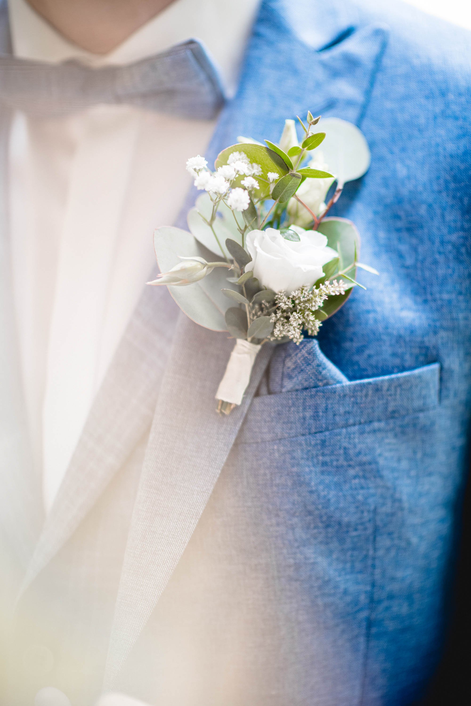 Nahaufnahme eines Anzugs mit Blumenspray aus weißen Blumen und grünen Blättern in der Brusttasche