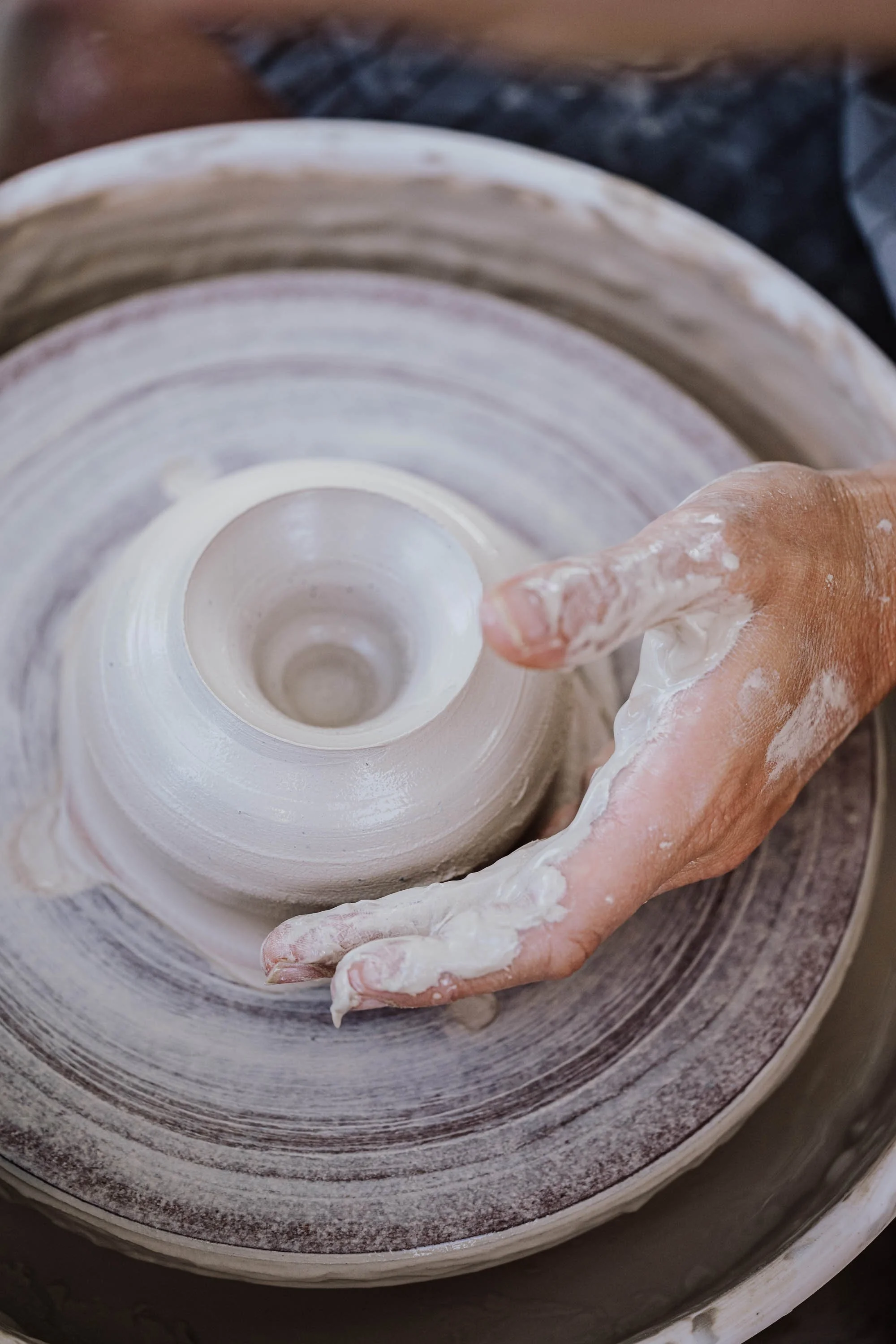 Nahaufnahme einer Hand, die auf einer Töpferscheibe Ton formt, um eine Vase zu erstellen, mit Abdrücken von Ton an den Fingern.
