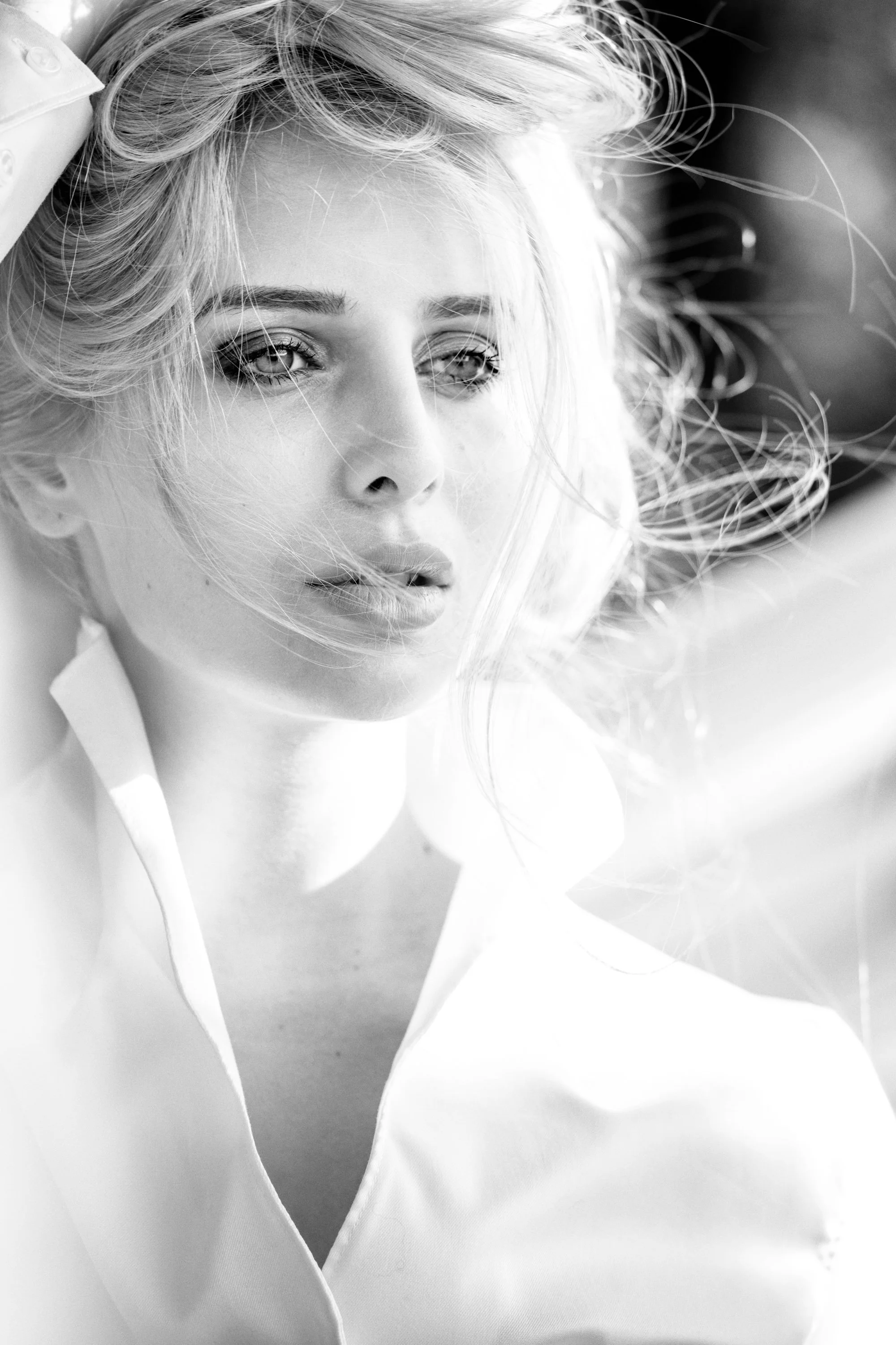 Schwarz-weiße Nahaufnahme einer jungen Frau mit lockigem Haar, die nachdenklich schaut.