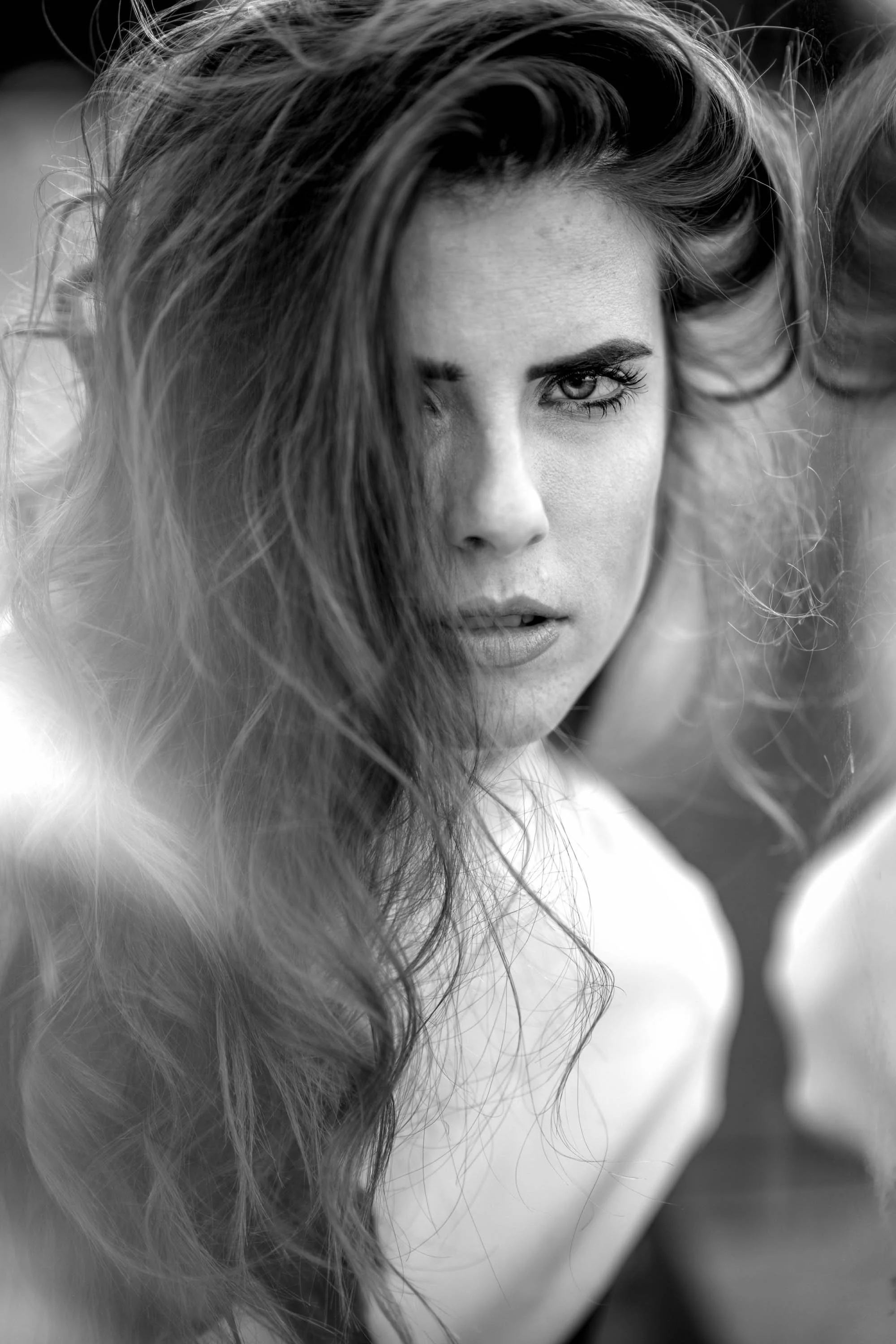 Schwarz-weiß Fotografie eines jungen Frauengesichts mit voluminösem, lockigem Haar, intensiven Blick und leicht geöffnetem Mund.