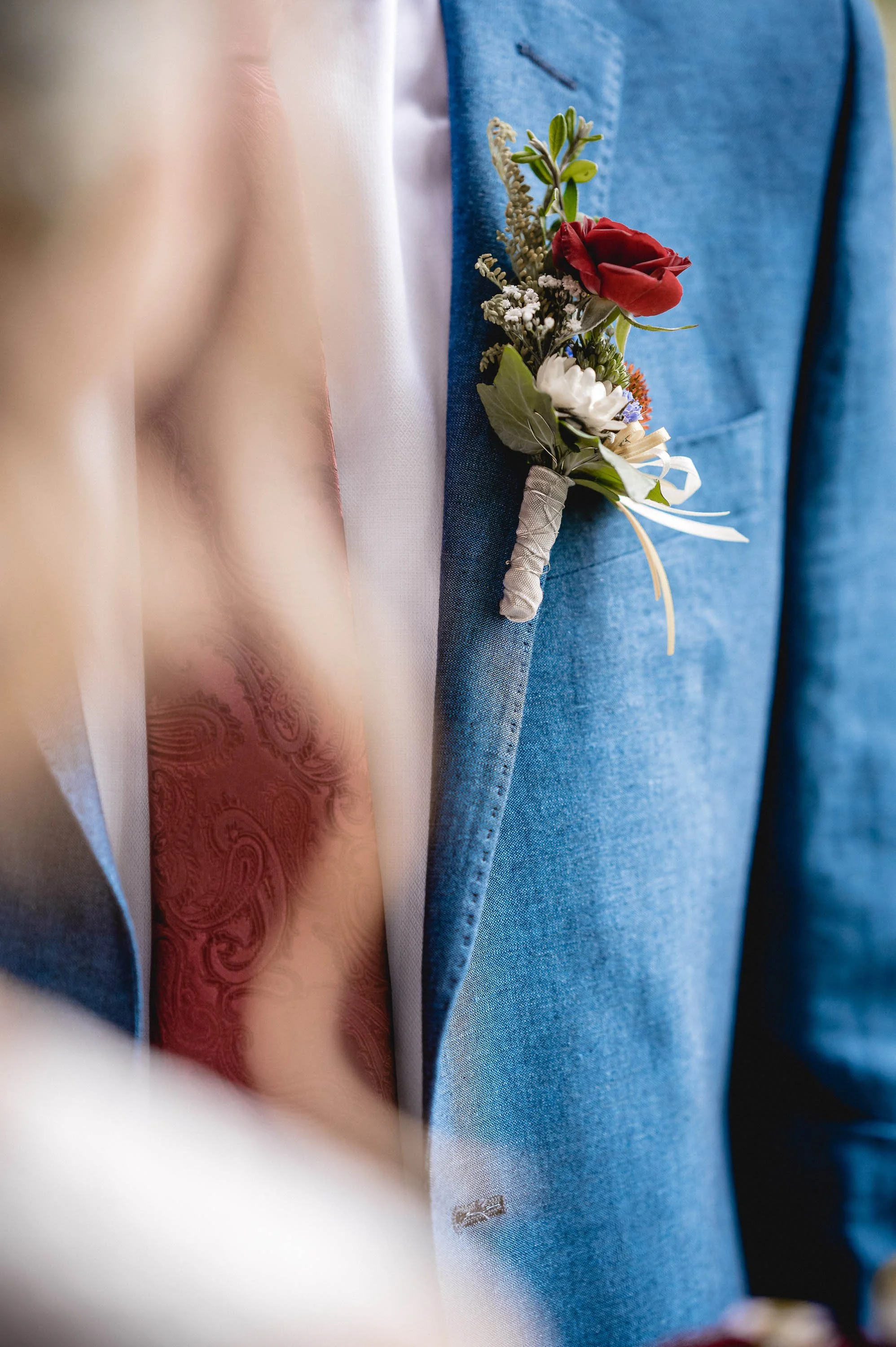 Nahaufnahme eines blauen Anzugs mit einer Hochzeitsblume im Revers, bestehend aus roten und weißen Blumen mit grünen Blättern.