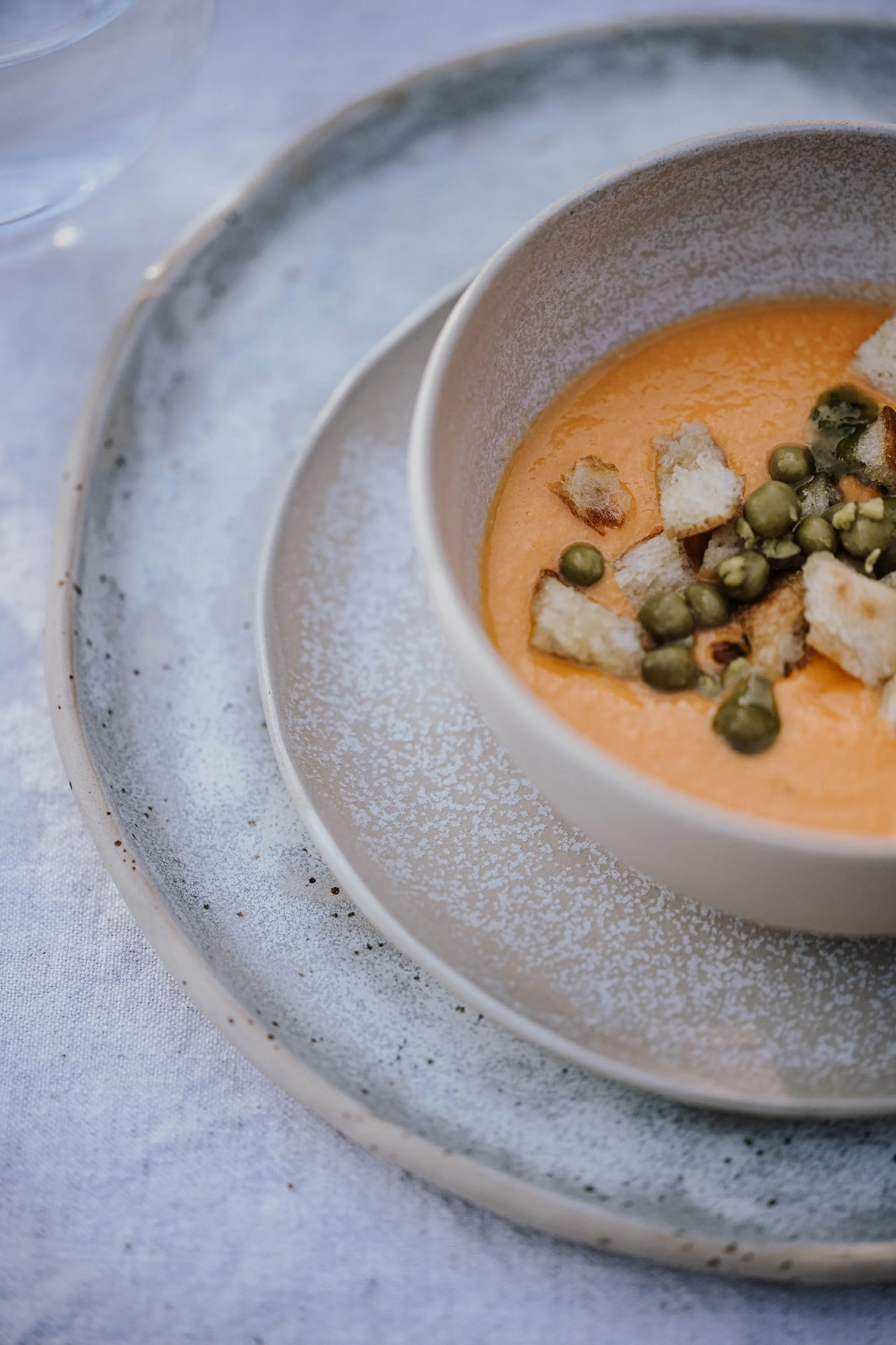 Eine Pizza in einer Backform mit Oliven, Tomaten und Kräutern, auf einem Tisch mit verschiedenen Beilagen und Getränken.