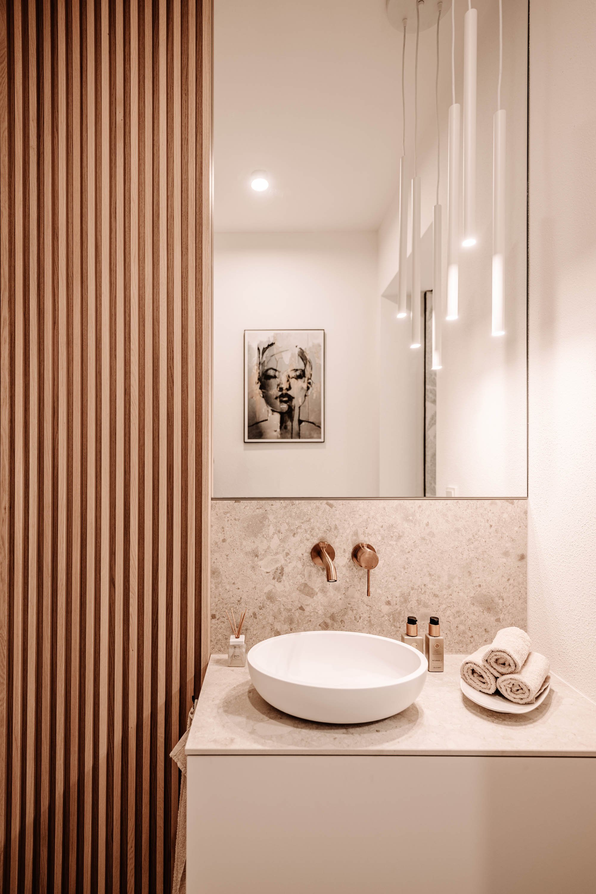 Moderne Badezimmer mit ovalem Waschbecken, gestreiftem Holzrahmen, Spiegel und Wandlampen, Wandkunst eines Portraits.