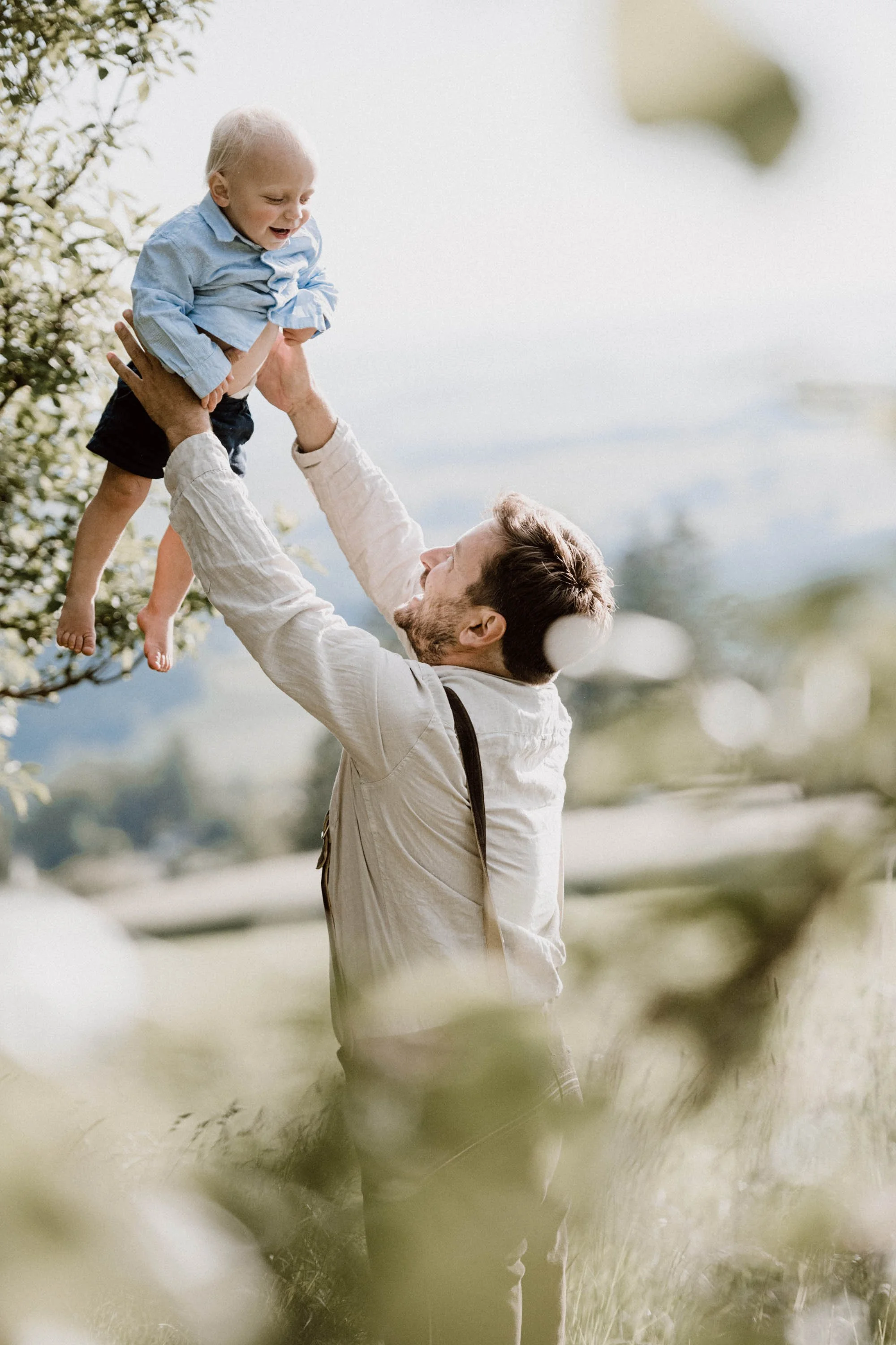 Vater hebt kind lachend in der Natur hoch.