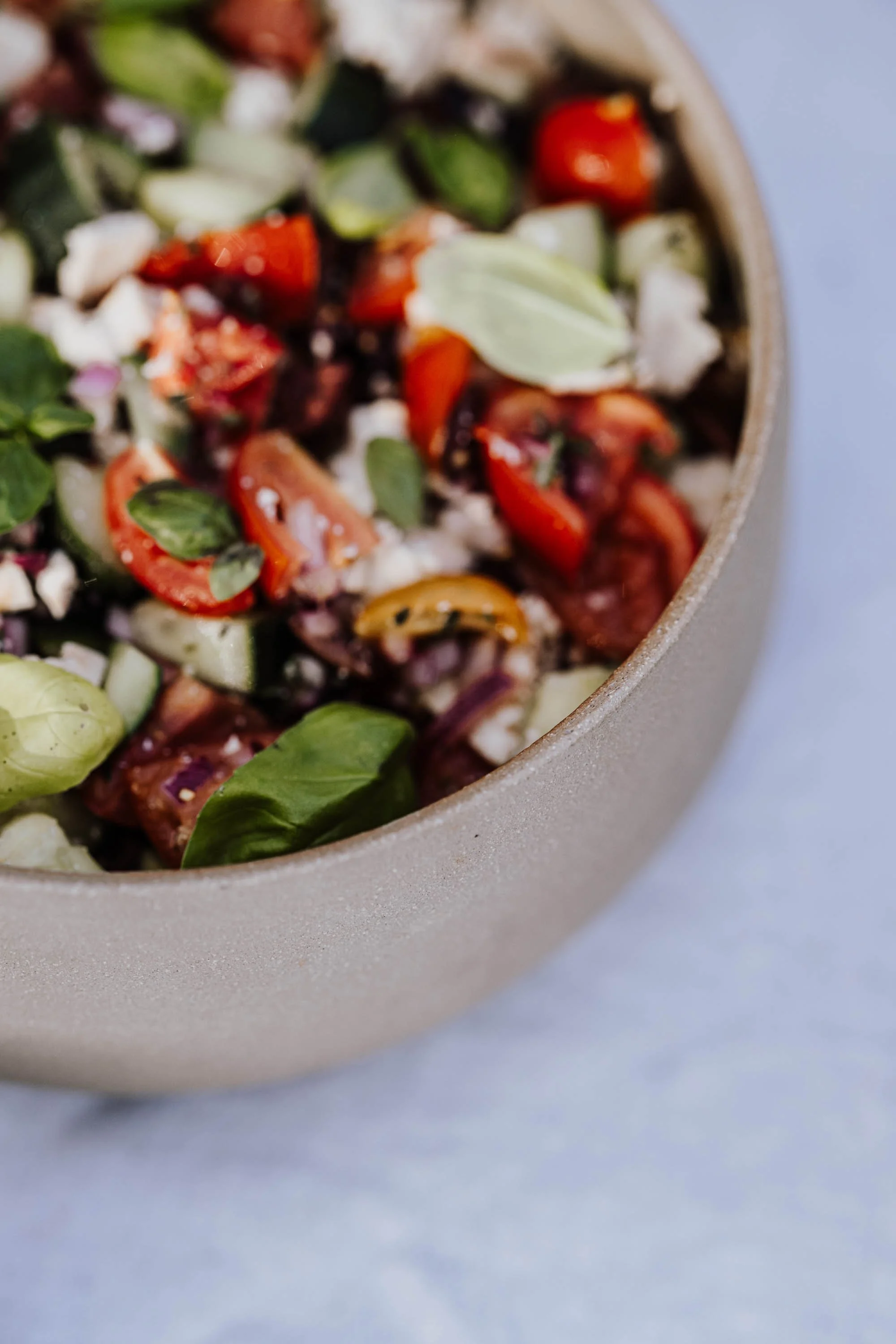 Bunter Gemüsesalat in einer grauen Schüssel, enthält Tomaten, Gurken, Basilikum und Zwiebeln