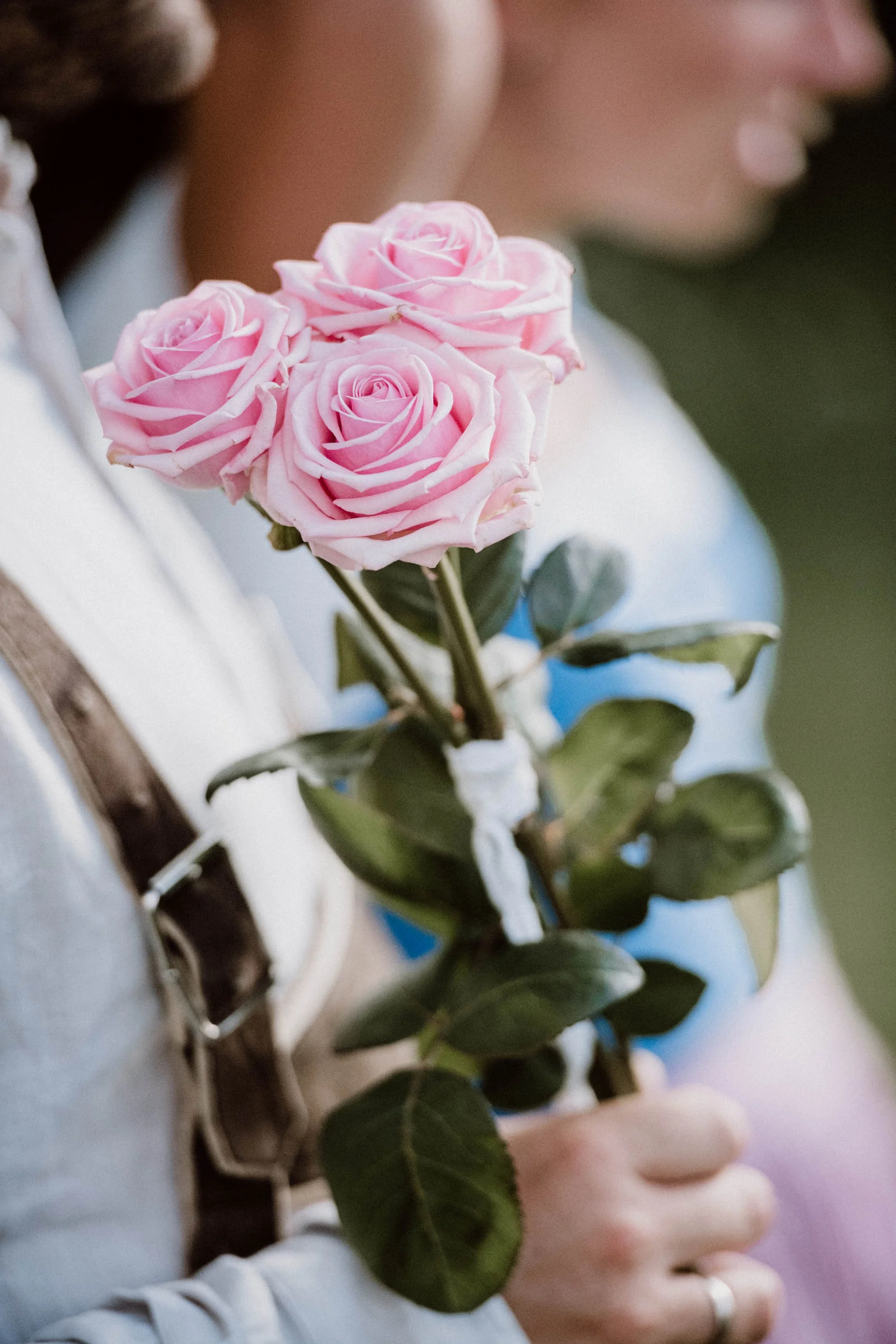 Person hält einen kleinen Blumenstrauß mit drei pinken Rosen und grünen Blättern.