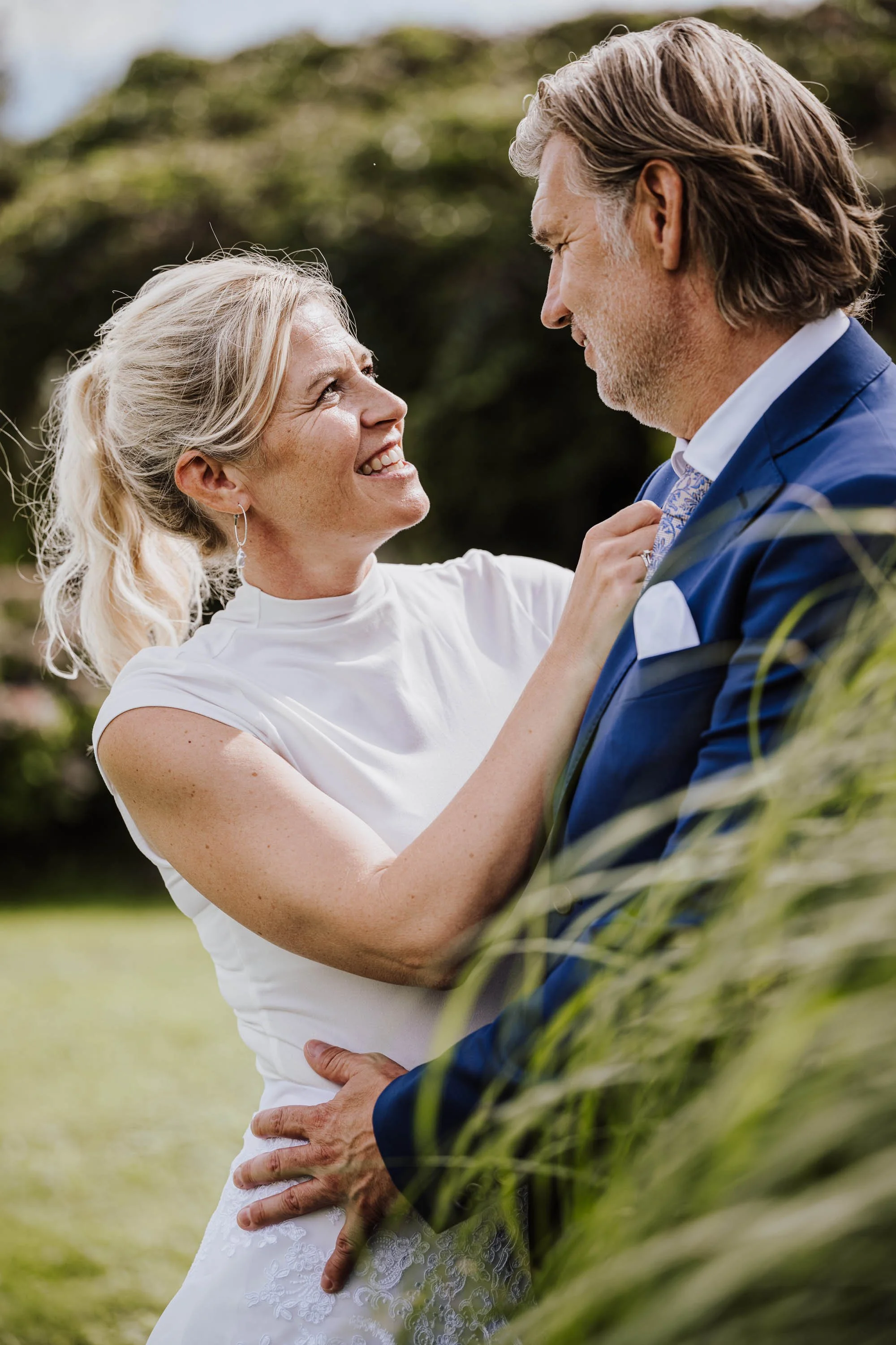Ein Paar in formeller Kleidung, die sich liebevoll im Freien gegenüberstehen, lächelnd und Händchen haltend.