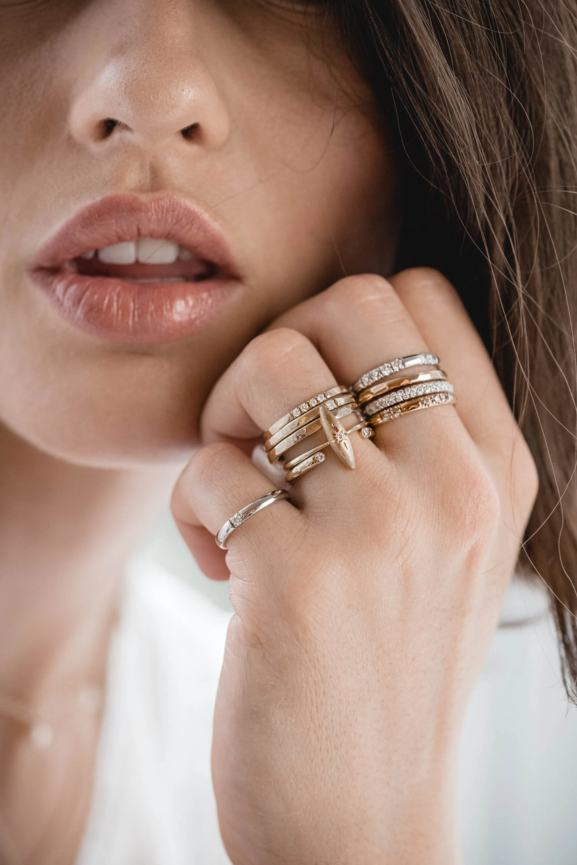 Nahaufnahme eines Mundes und einer Hand mit mehreren Ringen, der Frau trägt mehrere goldene und silberne Ringe mit Diamanten an der Hand