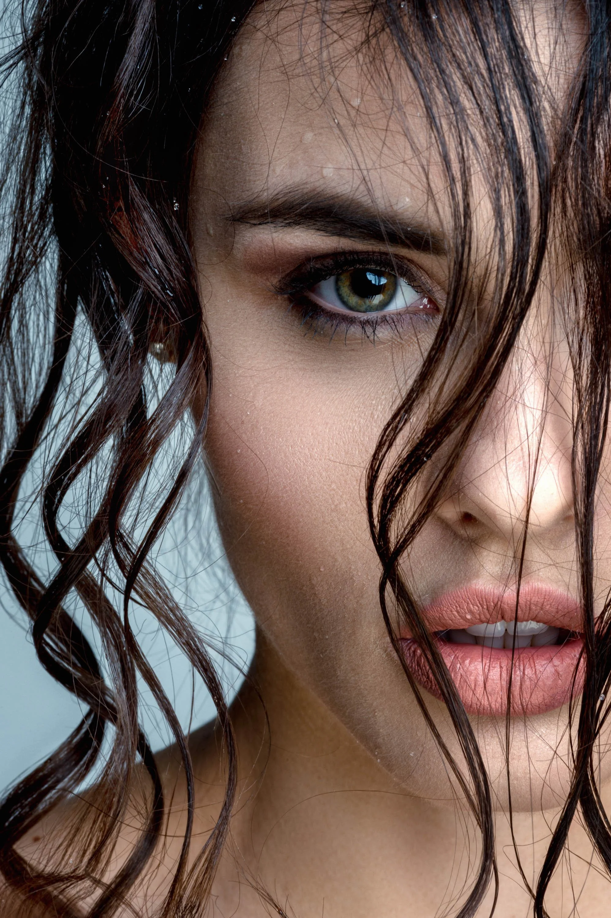 Nahaufnahme eines Gesichts mit grünen Augen, nassen dunkelbraunen, gewellten Haaren, feuchter Haut, leicht geöffnetem Mund und sichtbarem Lippenbeken.