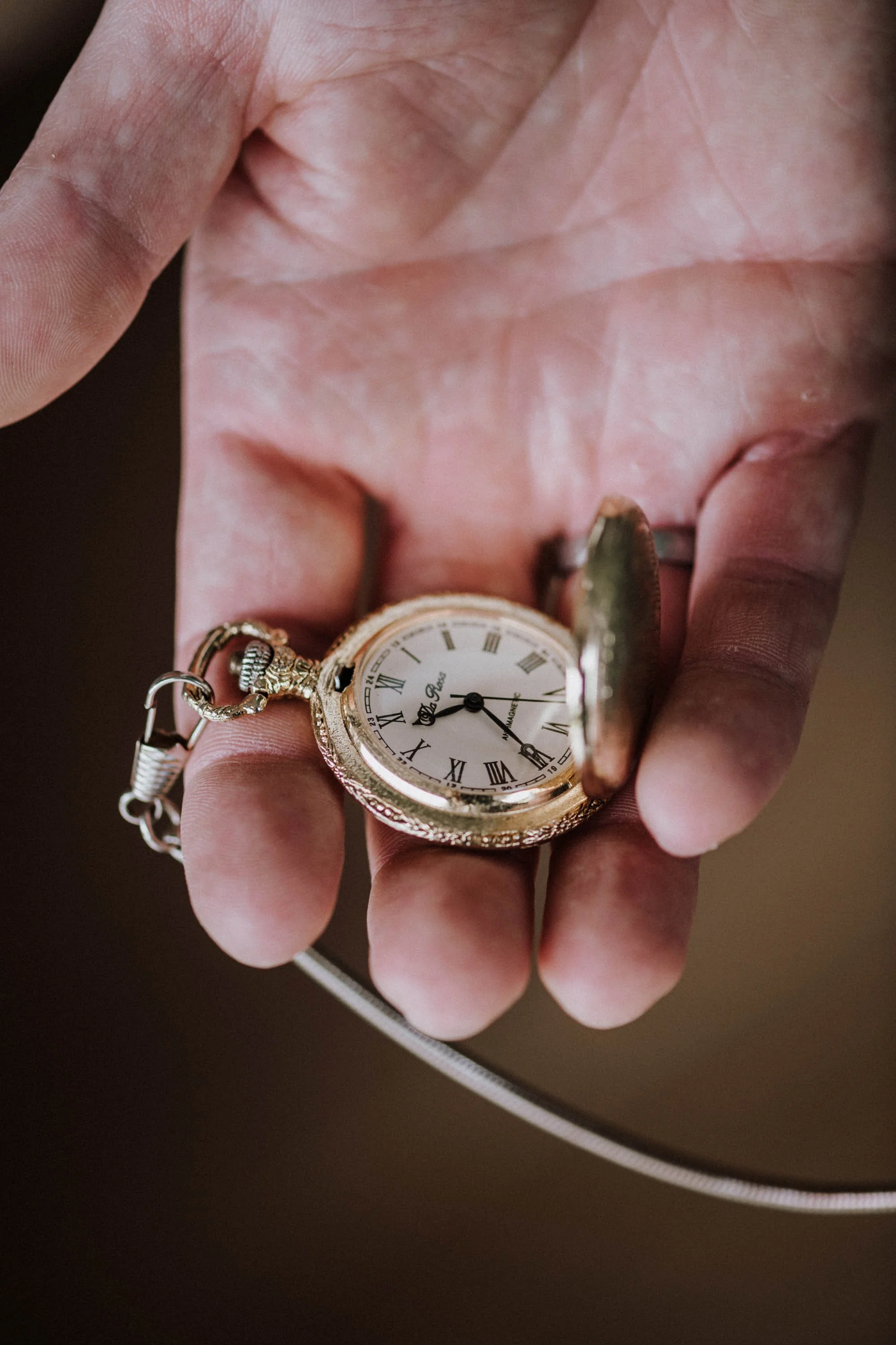 Eine Hand hält eine goldene Taschenuhr mit offenem Deckel, die Zifferblatt zeigt römische Zahlen und die Uhrzeit ist 8:22.