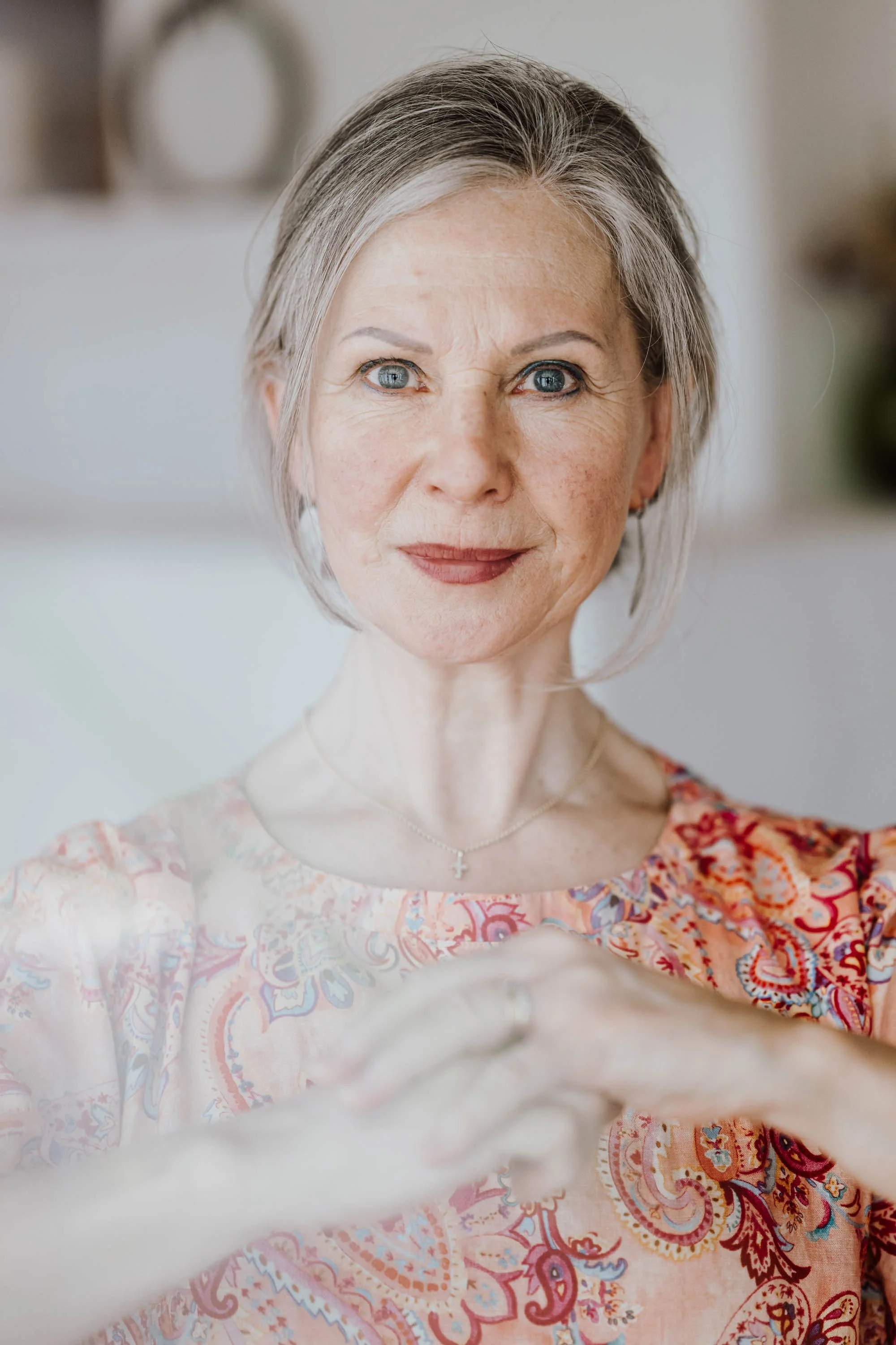 Nahaufnahme einer älteren Frau mit grauen Haaren, die ein Lächeln zeigt und ein Handy für ein Selfie verwendet.