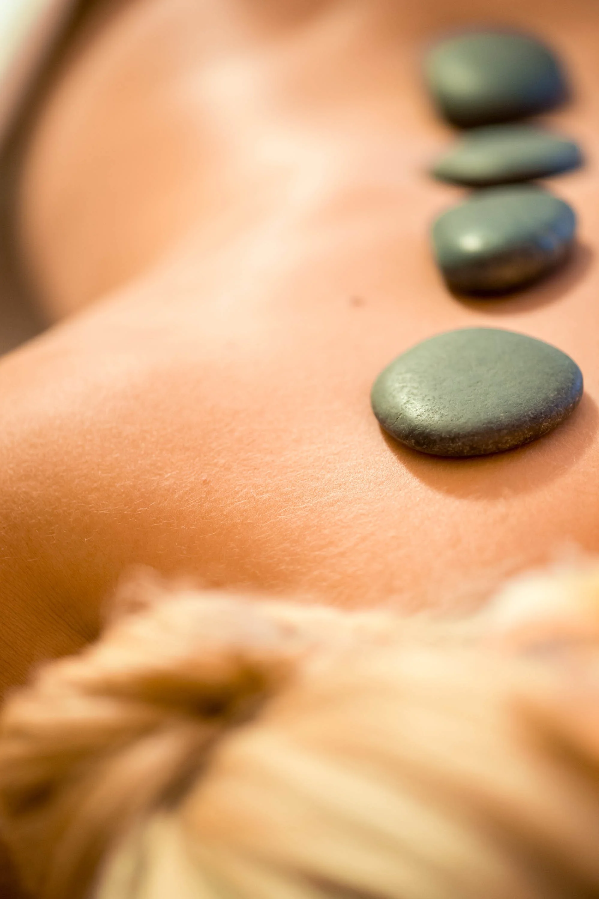 Nahaufnahme von vier flachen, grauen Steinen, die in einer Linie auf einer ovalen, orangefarbenen Oberfläche liegen.