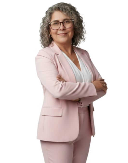 Mujer mayor con gafas, cabello rizado y canoso, vestida con traje rosa claro y camiseta blanca, con los brazos cruzados y sonriendo.
