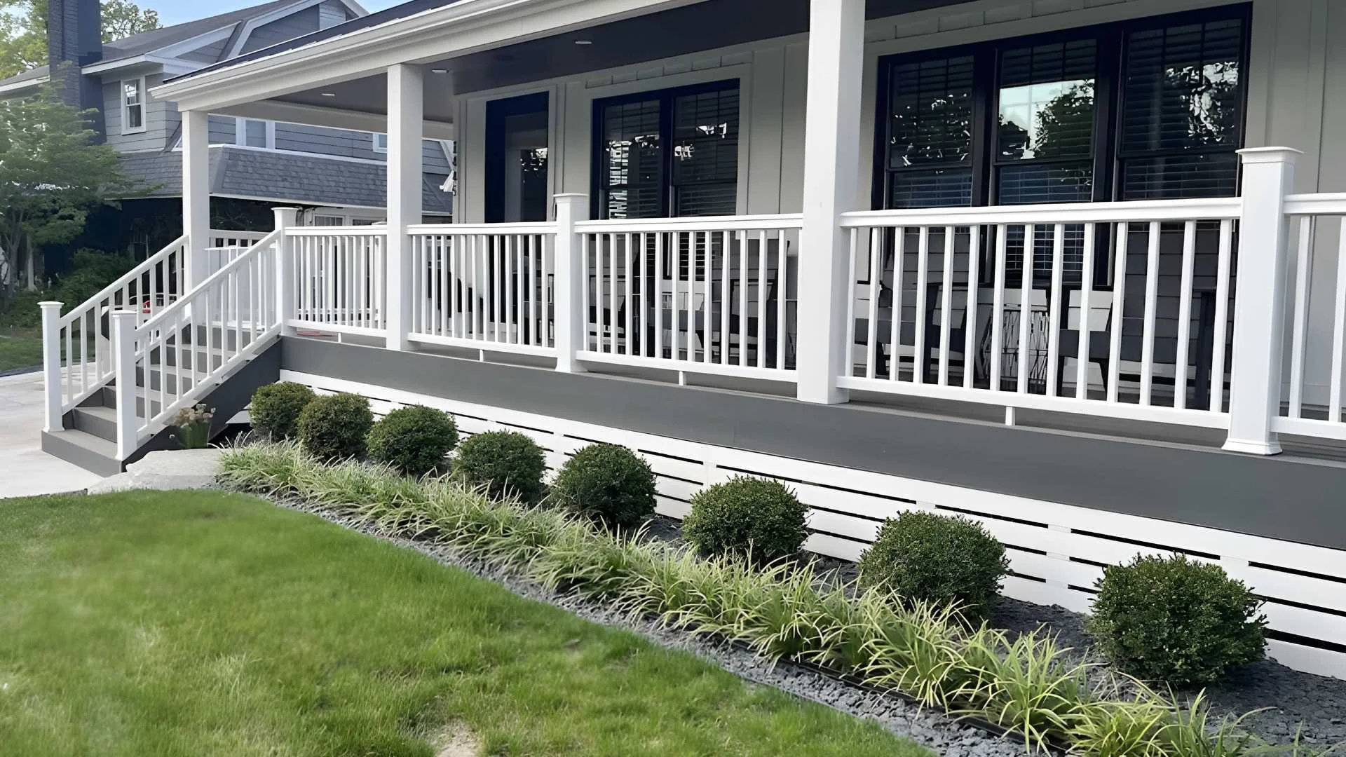 Front porch of a house with white railings, steps, and bushes along the foundation, with green lawn in front.
