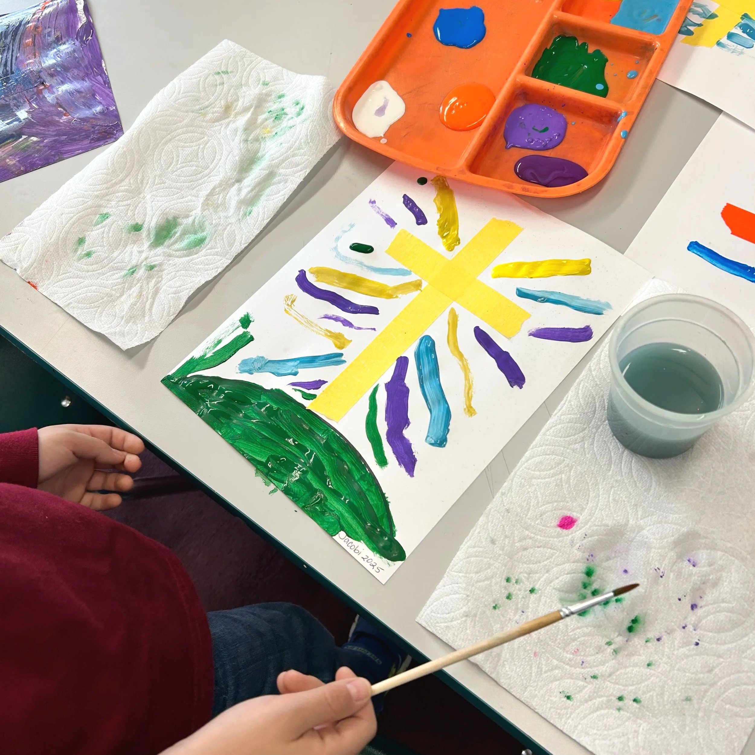 A preschool child holding a paintbrush draws a colorful gold cross