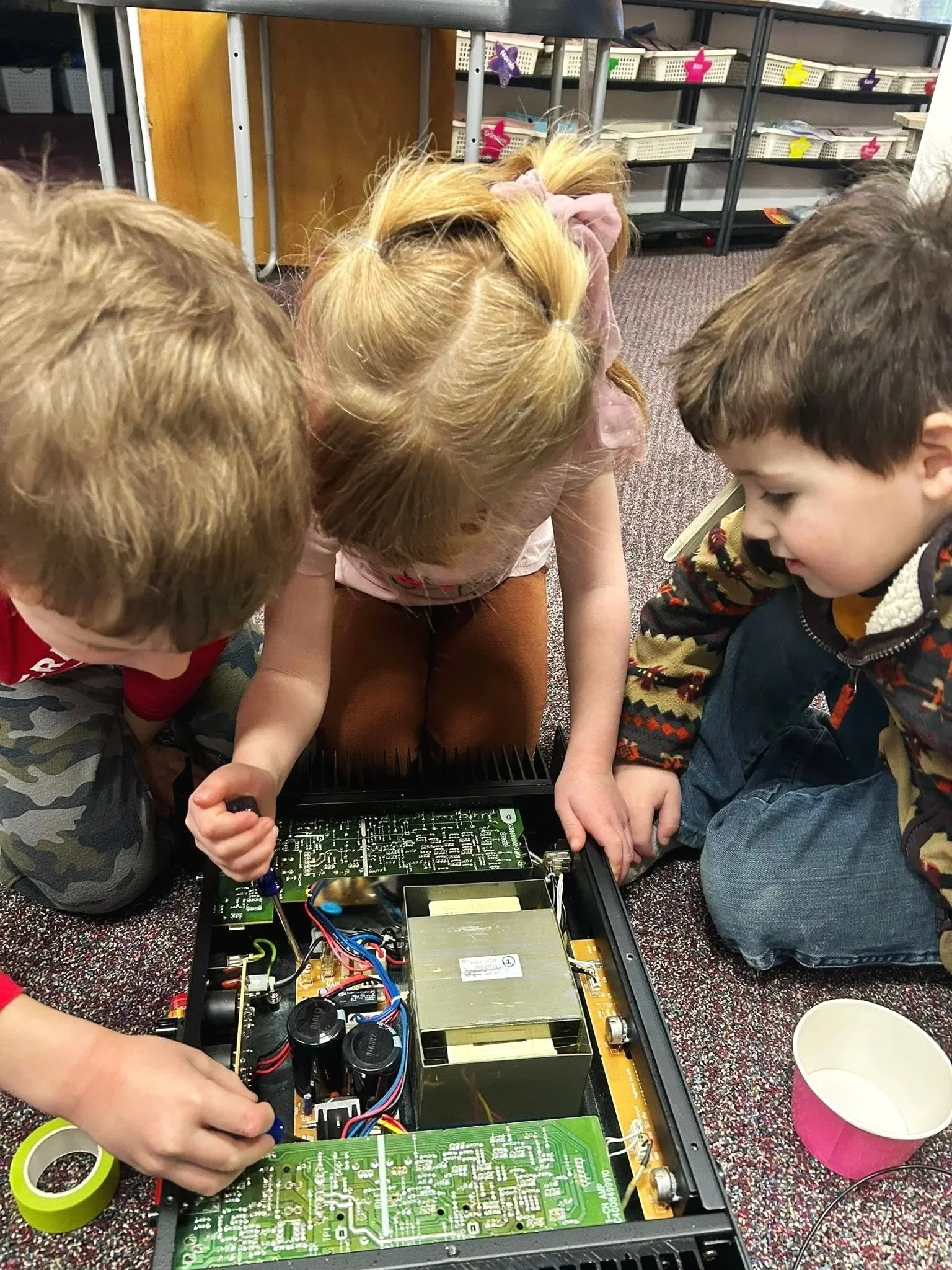 Three preschool children getting hands-on learning with an old computer motherboard