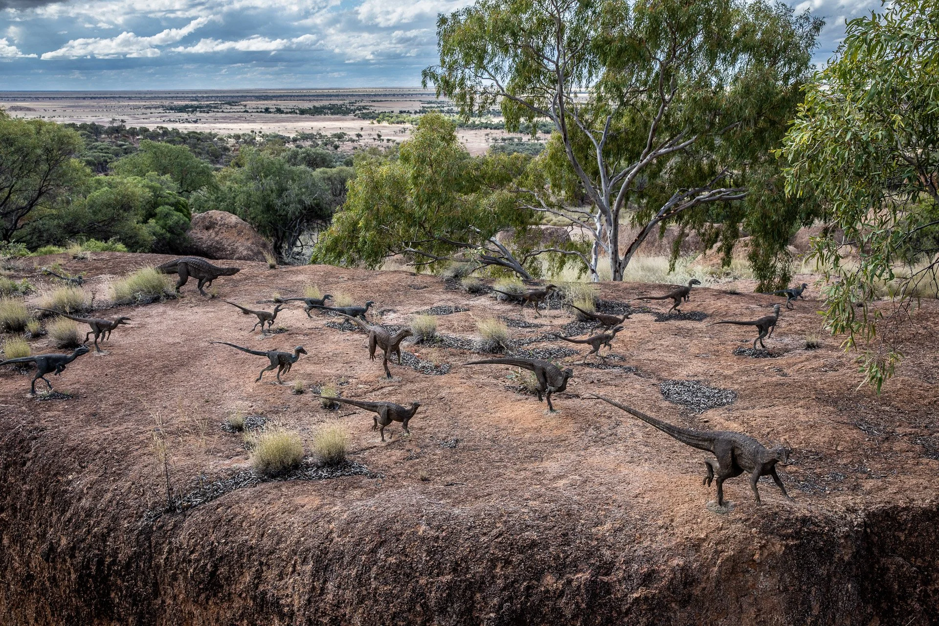 A miniature diorama of a desert landscape with model dinosaurs and trees.