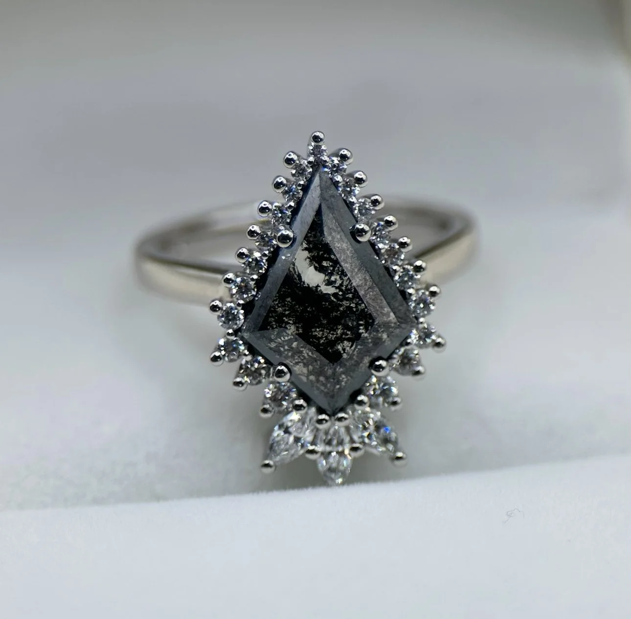 Silver ring with a large diamond-shaped black gemstone surrounded by smaller diamonds, set on a white background.
