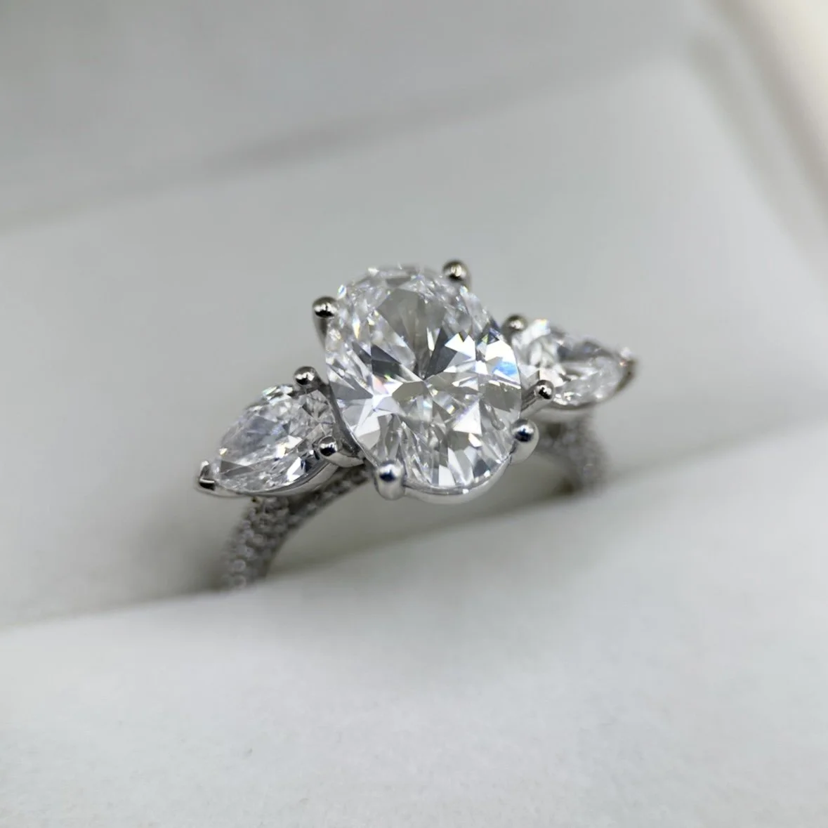 Close-up of a silver ring with a large oval-shaped diamond in the center, flanked by two pear-shaped diamonds, set against a white background.