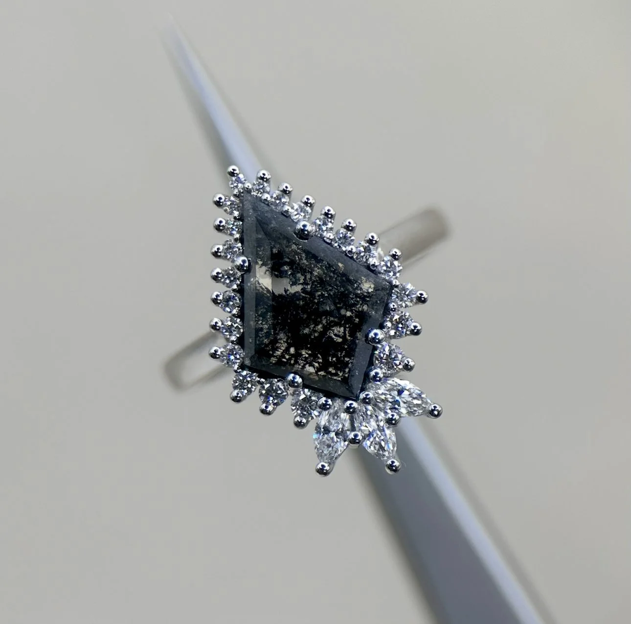 Silver ring with a large rectangular black gemstone surrounded by small diamonds on a white surface.