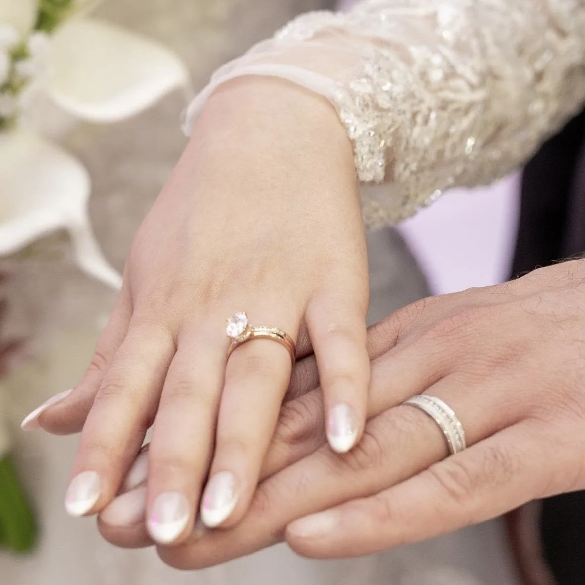 Close-up of a bride and groom holding hands, displaying their wedding rings.