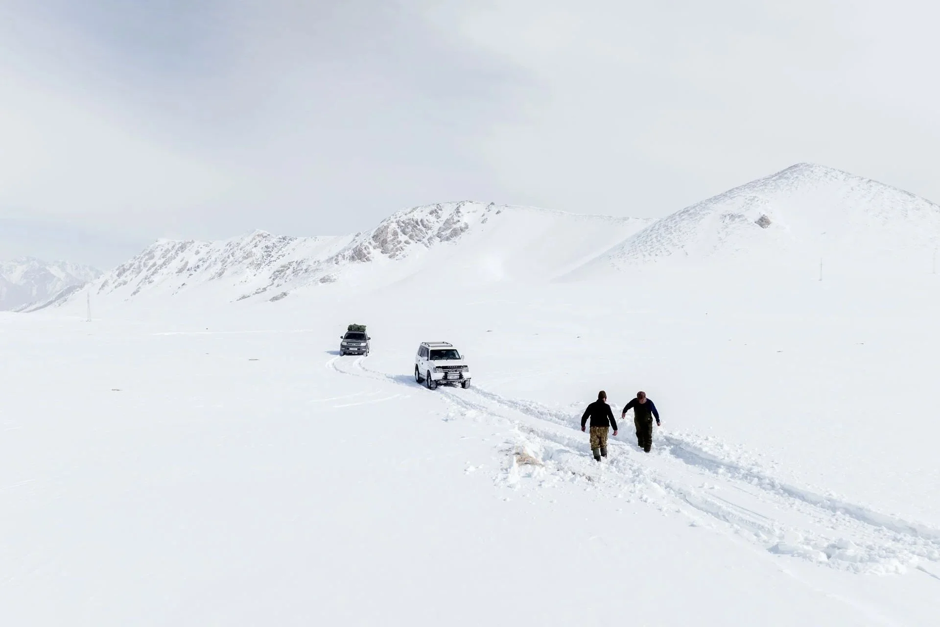 Two people walk through snow in the mountains of Kyrgyzstan tracking snow leopards