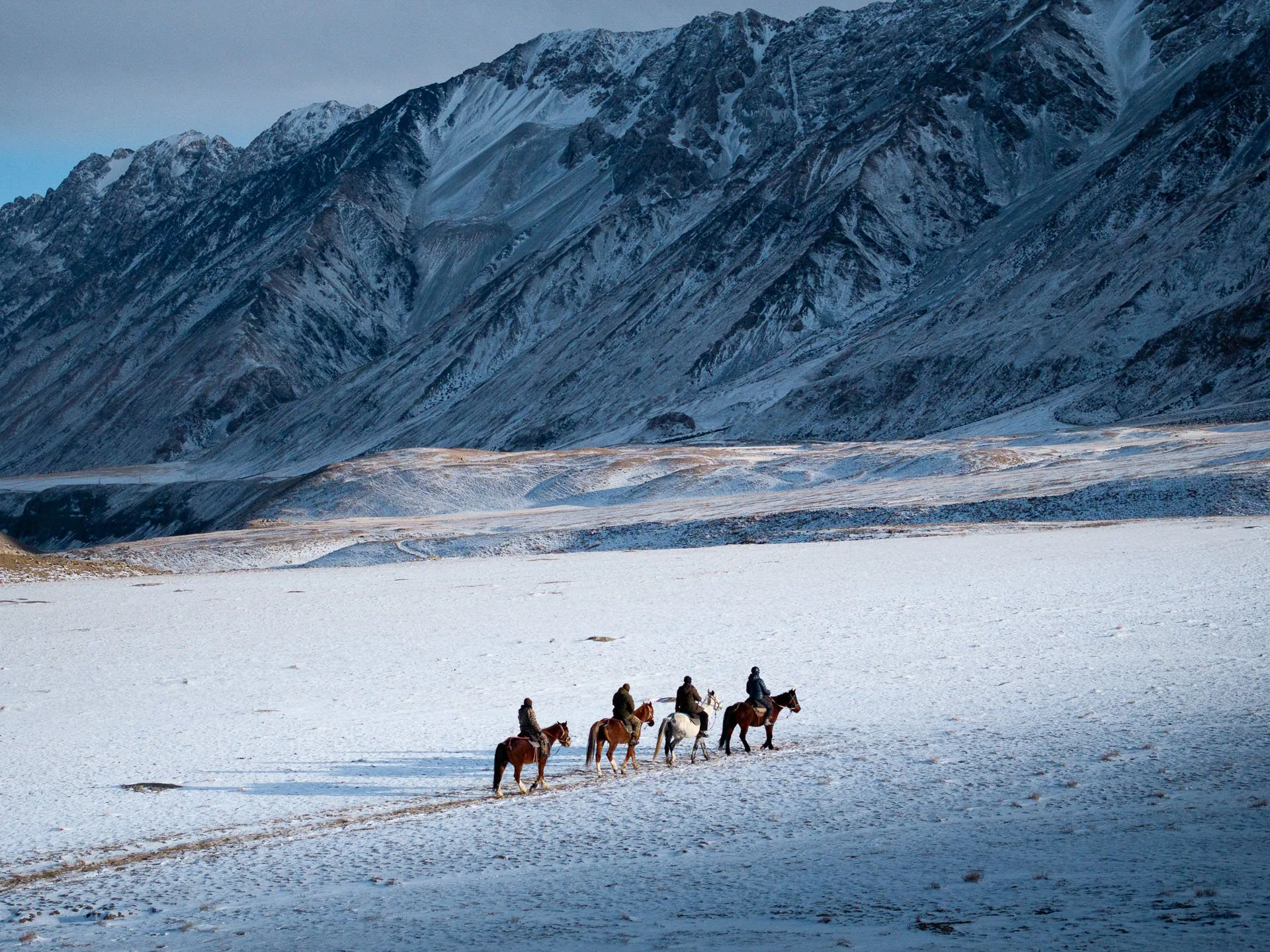 Horse riders in a snowy valley searching for snow leopards in Kyrgyzstan