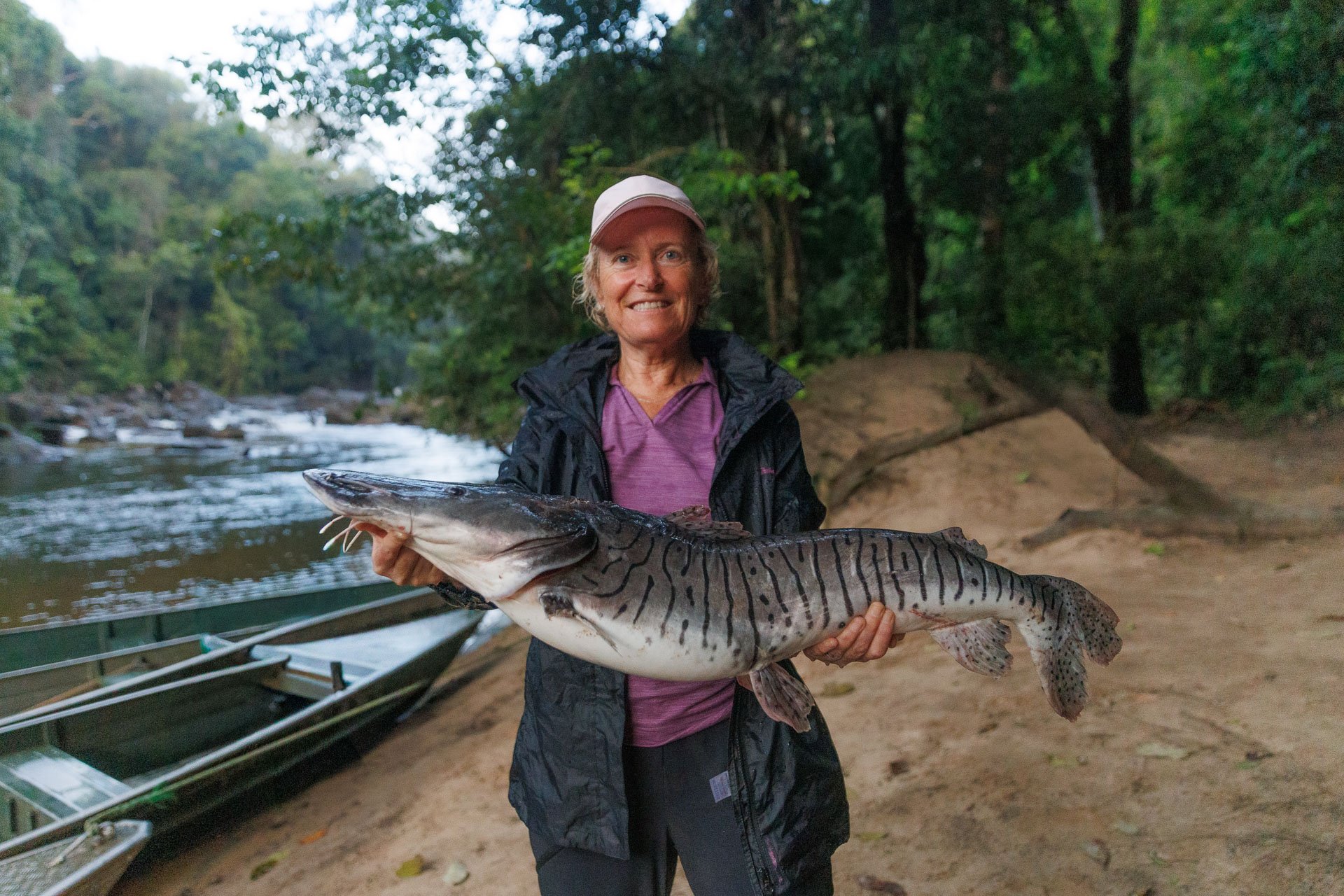 A woman holds a tiger fish in a remote camp location in the Guyana rainforest