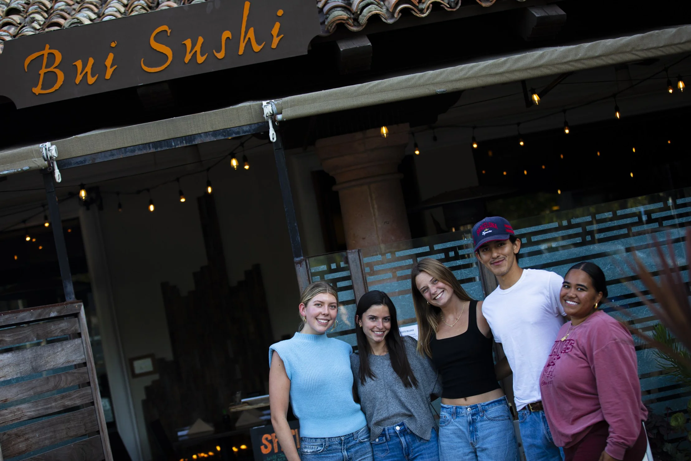 Group of five friends smiling outside a restaurant named Bui Sushi.