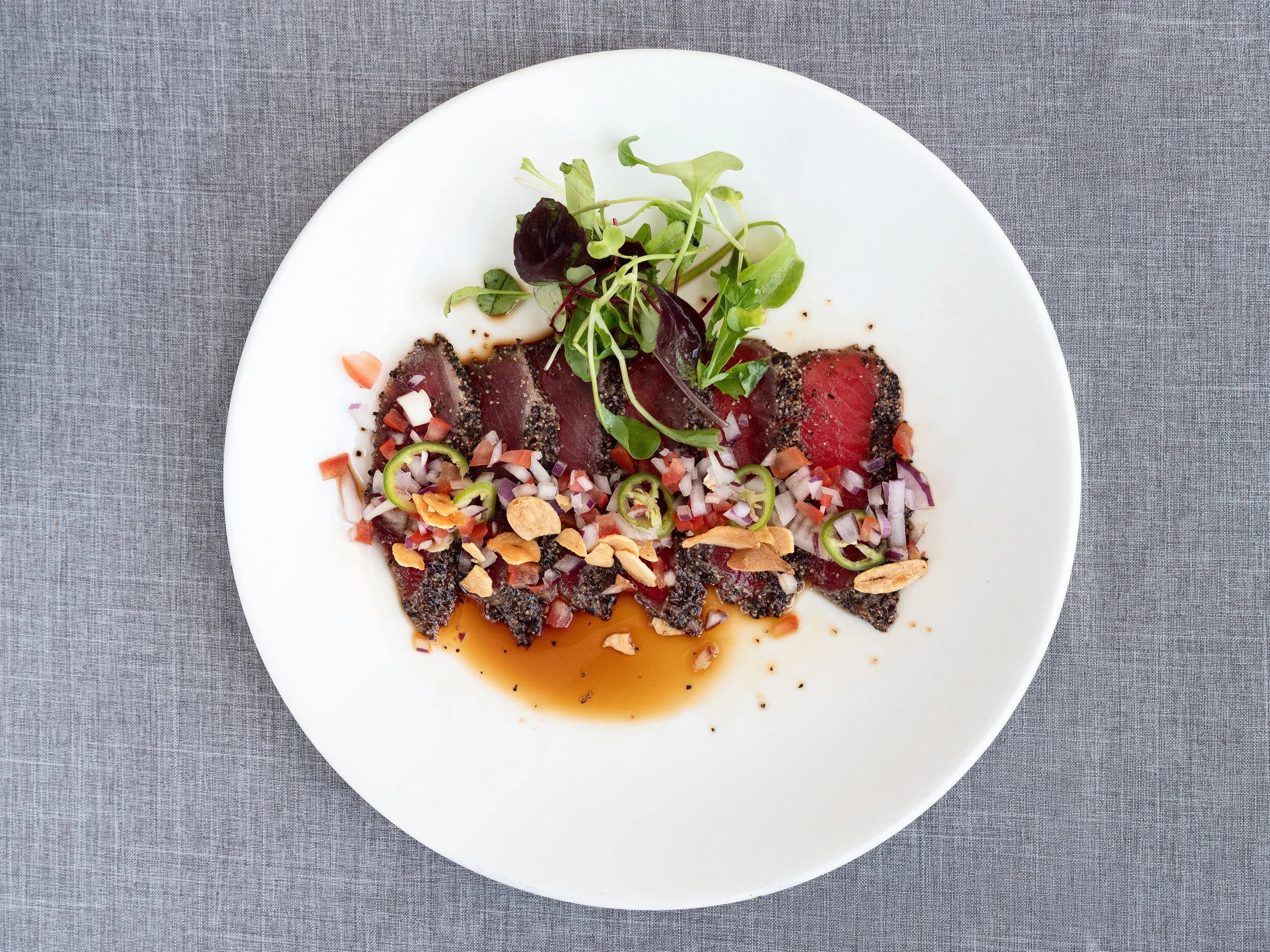 Sliced seared tuna with complementing garnishes and sauce on a white plate