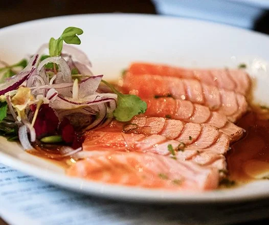 Sliced salmon with a side salad on a white plate.