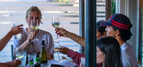 Group of people clinking glasses of white wine at a dining table.