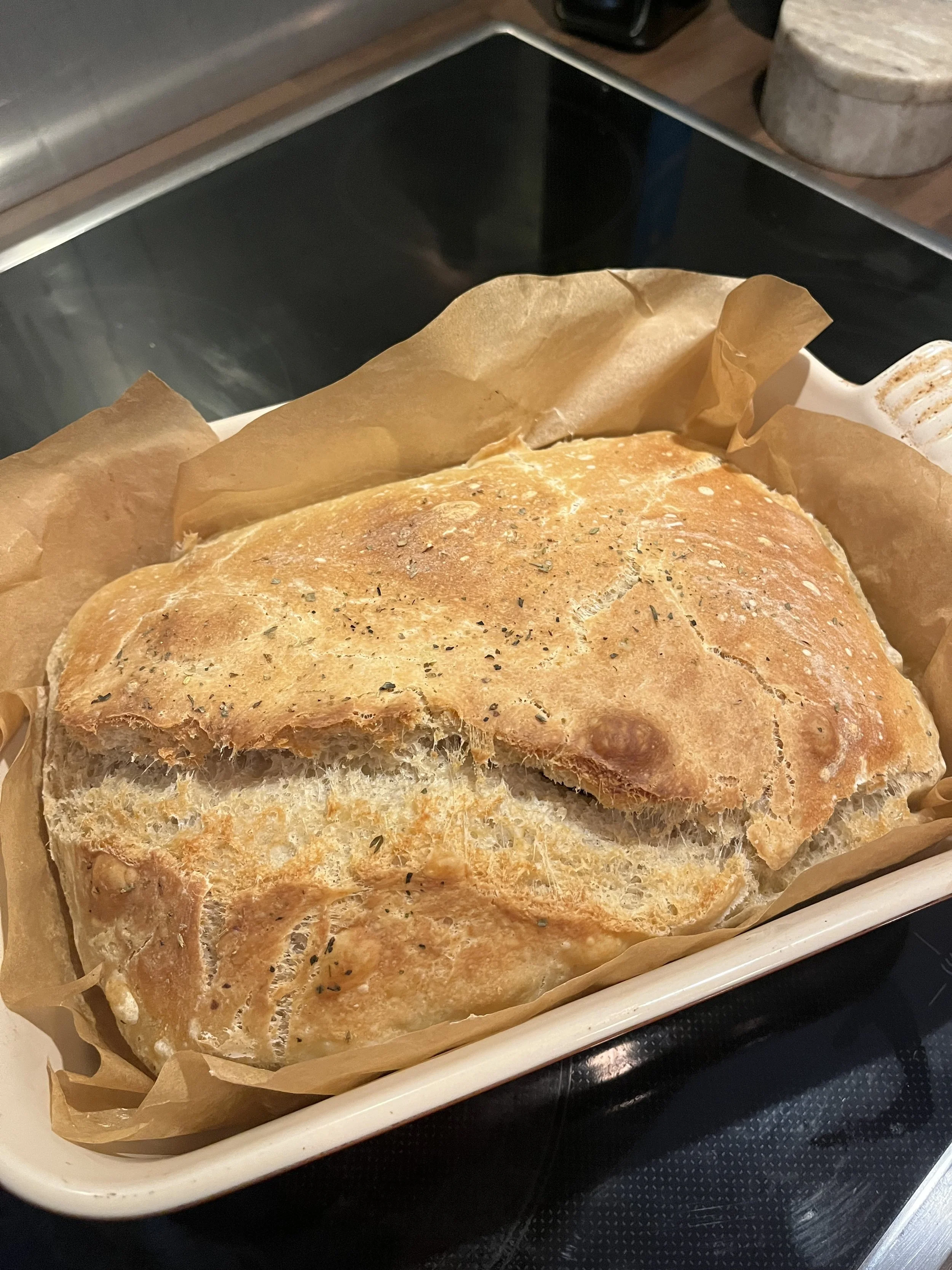Baked bread with herbs in a baking dish lined with parchment paper on an oven stove.