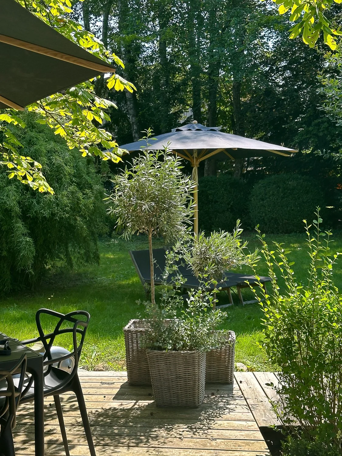 Garten mit Liegestuhl, Sonnenschirm, Pflanzkübel, Bistrotisch und Stühlen in sonnigem, grünen Garten.