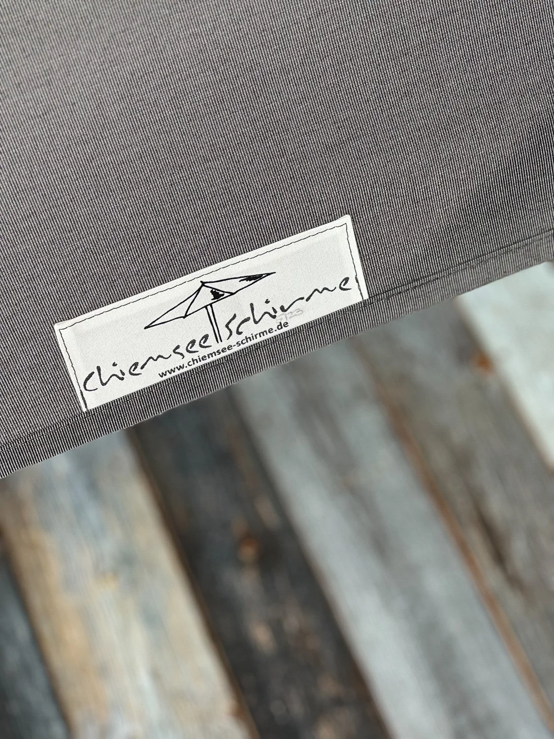 Nahaufnahme eines Stoffschilds mit dem Logo von Chiemsee Schirme auf einem Sonnenschirm.