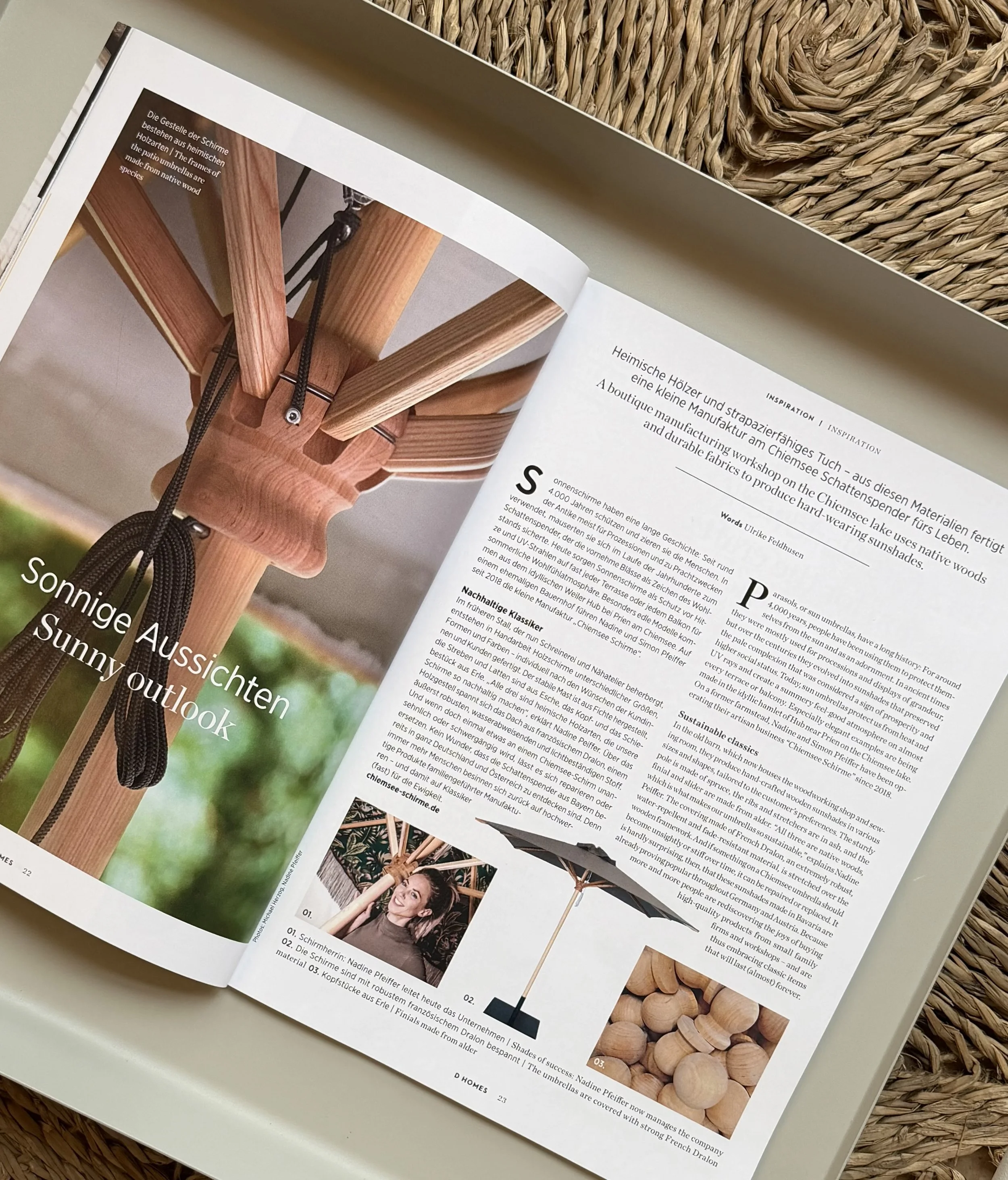 Offene Zeitschrift mit einem Porträt über Chiemsee Schirme, darunter ein Holzsonnenschirm vor einem natürlichen Hintergrund.