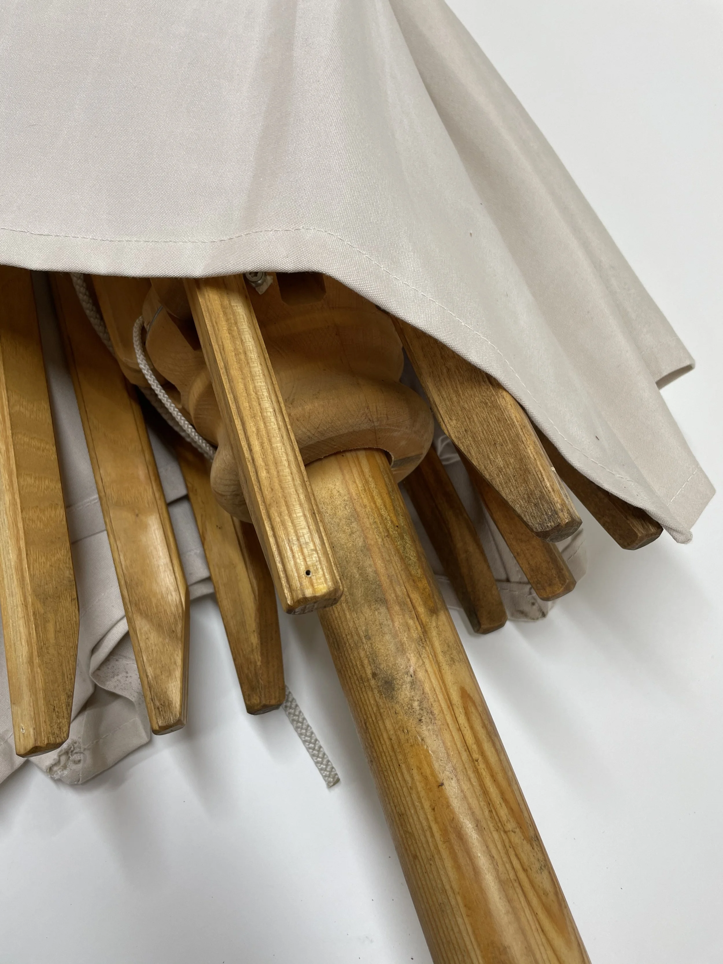 Blick auf die unteren Holzteile eines Sonnenschirms nach einem Sturmschaden, teilweise noch mit beigem Stoff bespannt.