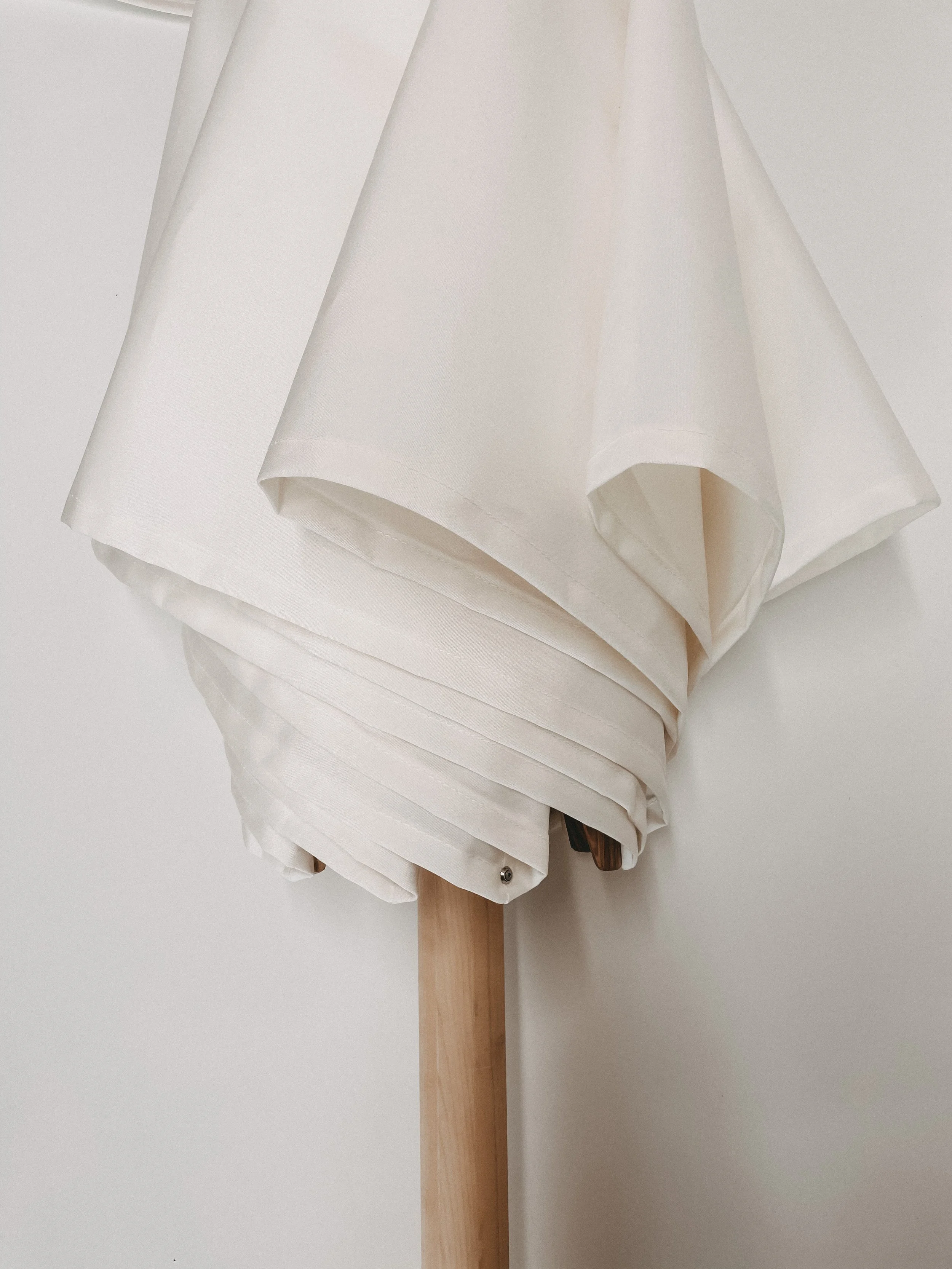 Ein weißer Sonnenschirm mit hölzernem Mast steht vor einer weißen Wand.