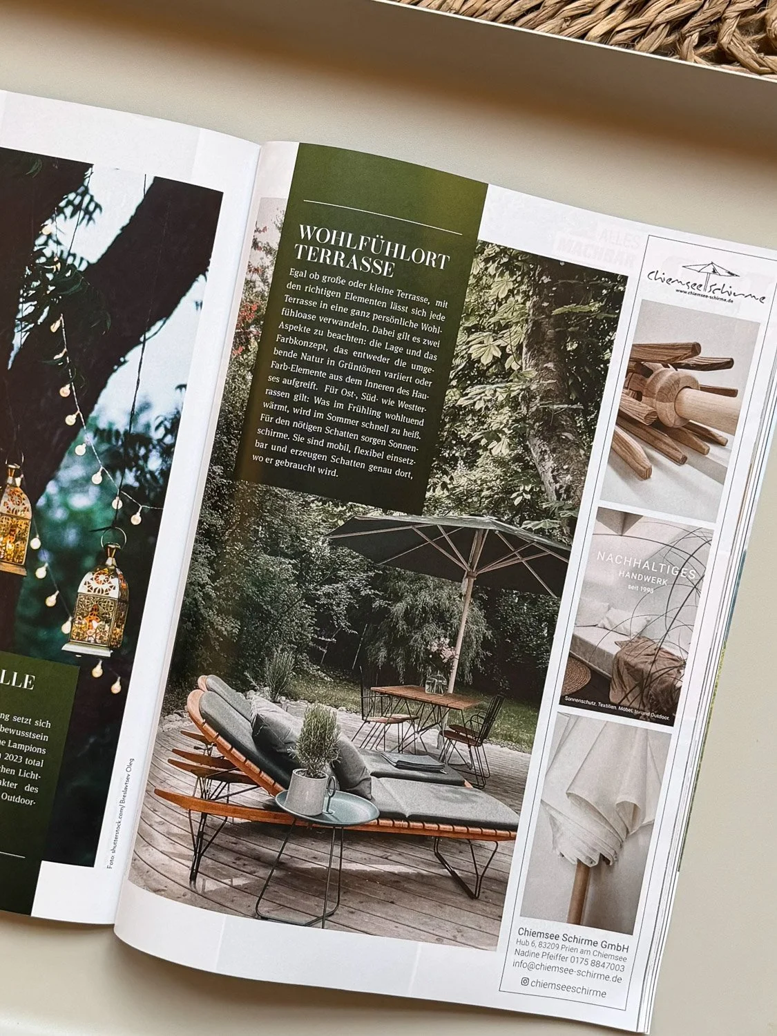 Eine Seite eines Magazins mit einem Bild eines Gartenmöbel-Setups mit hellgrauem Sonnenschirm, einem runden Tisch und mehreren Sesseln auf einer Holzterrasse umgeben von Bäumen.