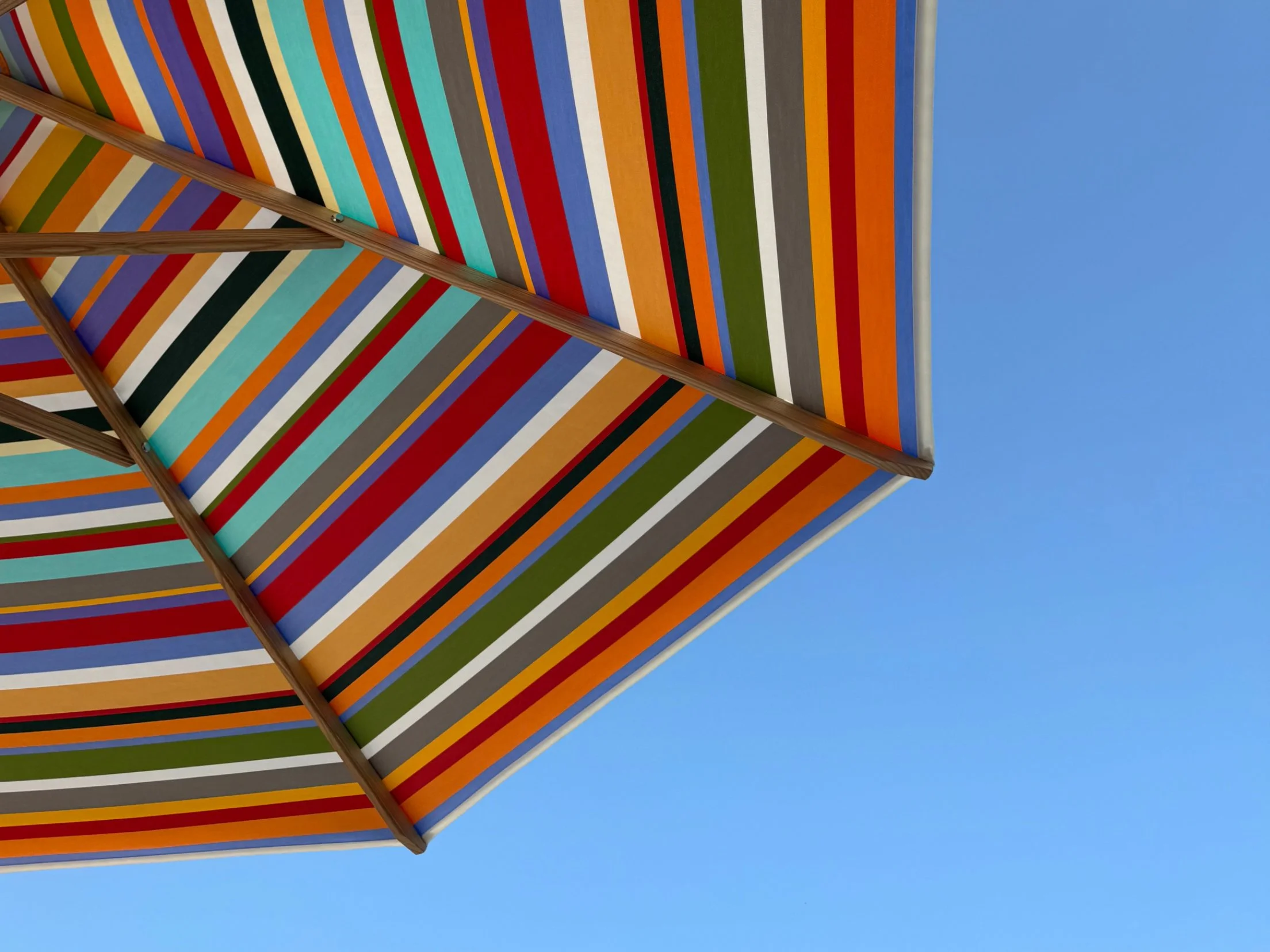 Bunter Sonnenschirm von Chiemsee Schirme mit Streifen in Rot, Grün, Blau, Orange, und Weiß unter blauem Himmel.