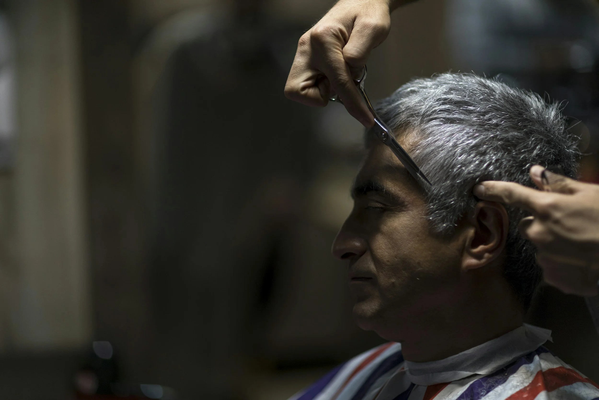 A person giving a haircut to an elderly man with gray hair.