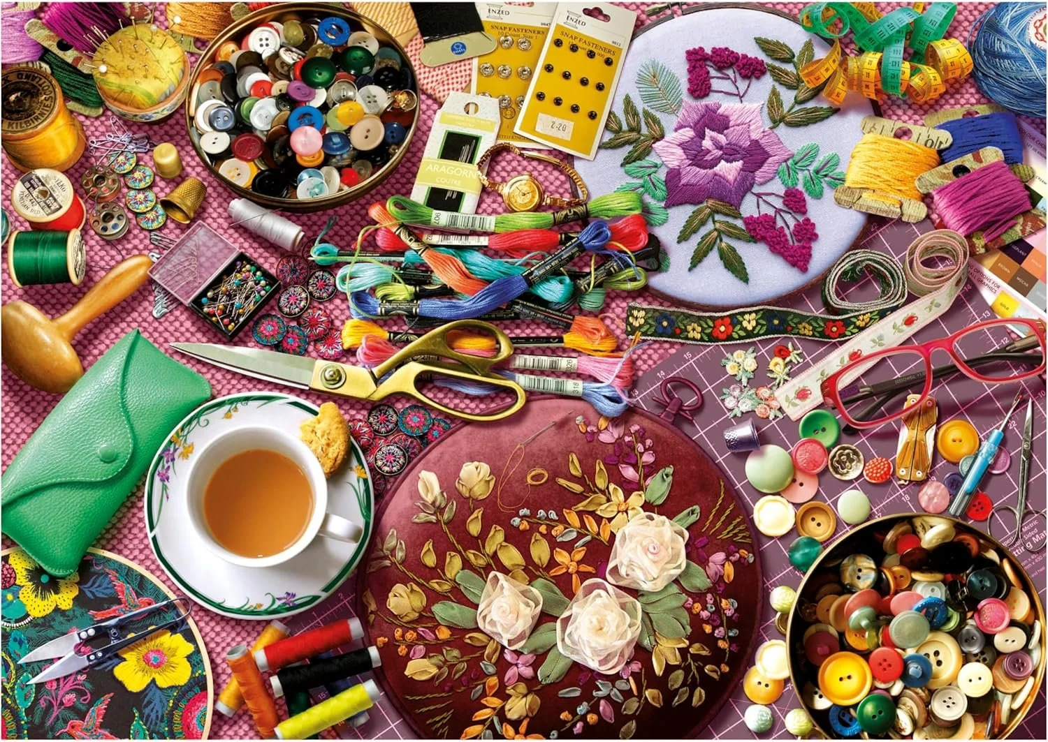 Diversen naaispulletjes, garen, knopen, scheermesje, schaar, borduurwerk, kleine accessoires, drinkkop met thee, brillen, meetlint, bloemen, en stoffen op een roze naaitafel.