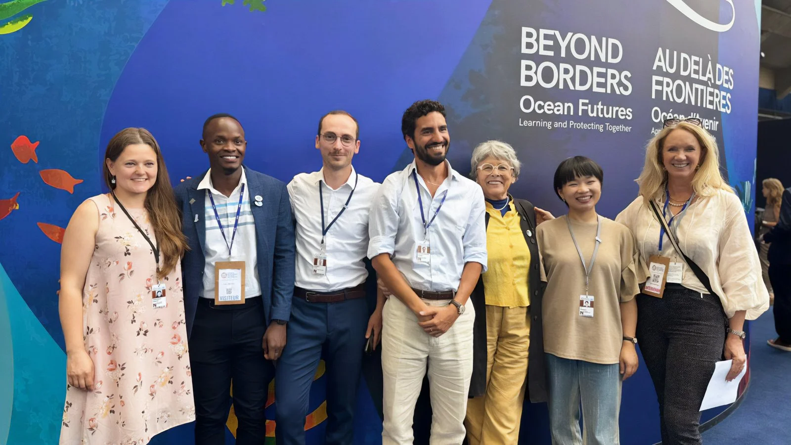 Group of seven diverse people smiling and posing at an event with a backdrop that reads 'Beyond Borders Ocean Futures Learning and Protecting Together'.