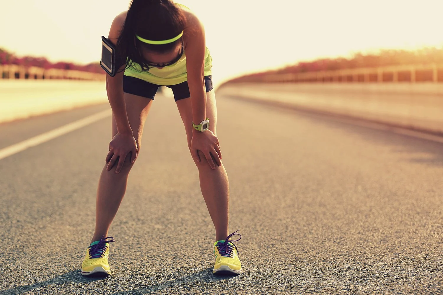 Atleta femminile stanca durante la corsa, piegato in avanti, su strada di campagna in luce solare.